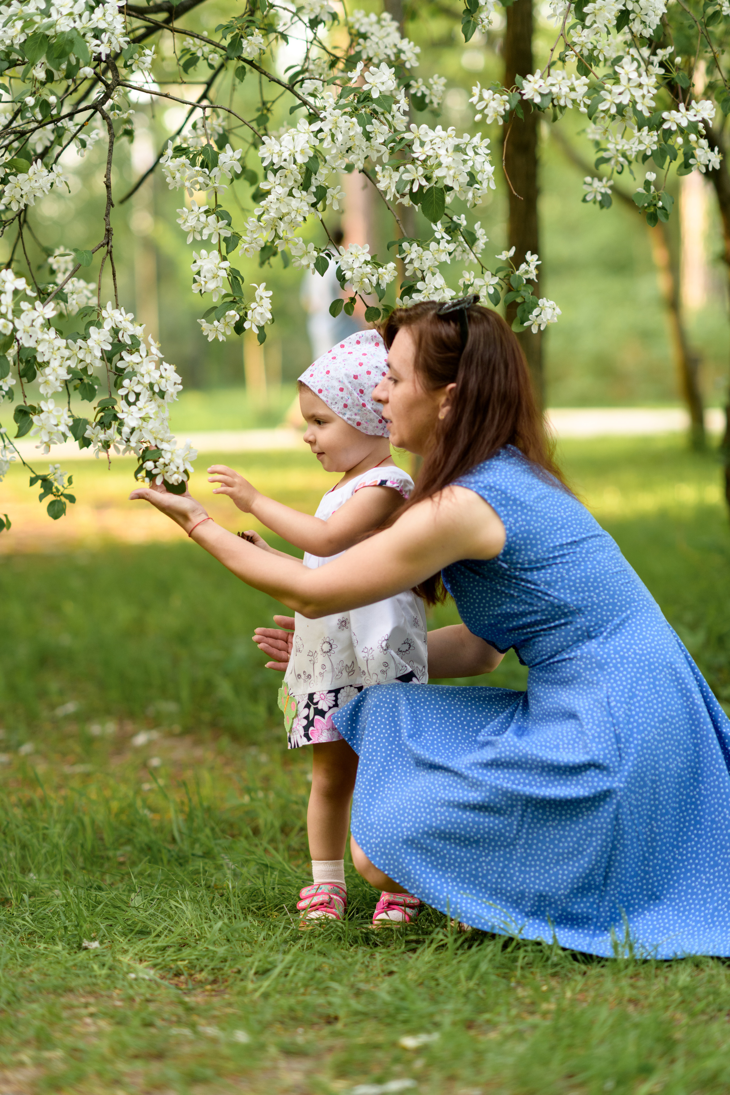 мама с дочкой рассматривают цветы на яблоне в парке