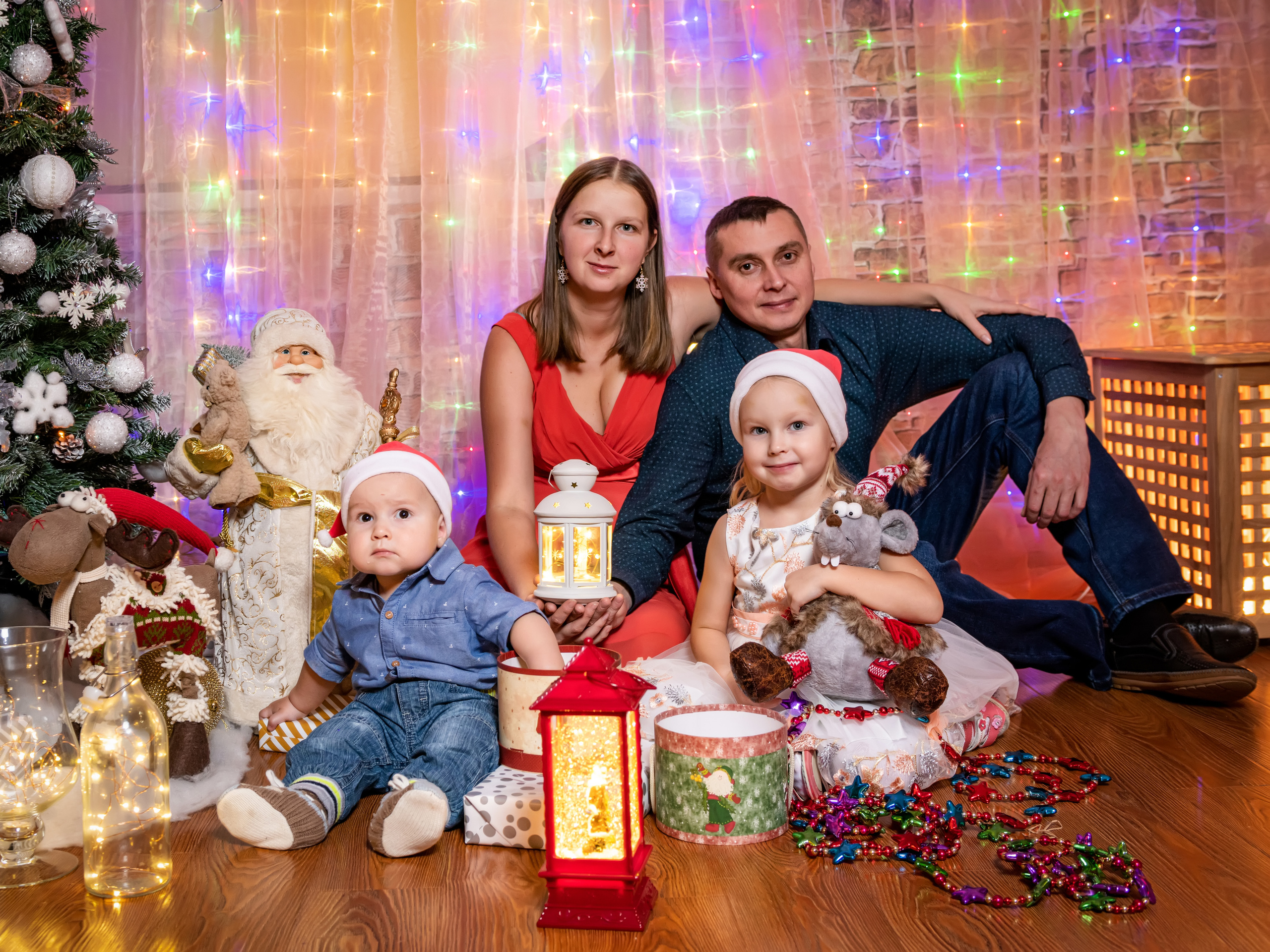 Семья сидит удобно устроившись на полу рядом с новогодней елкой