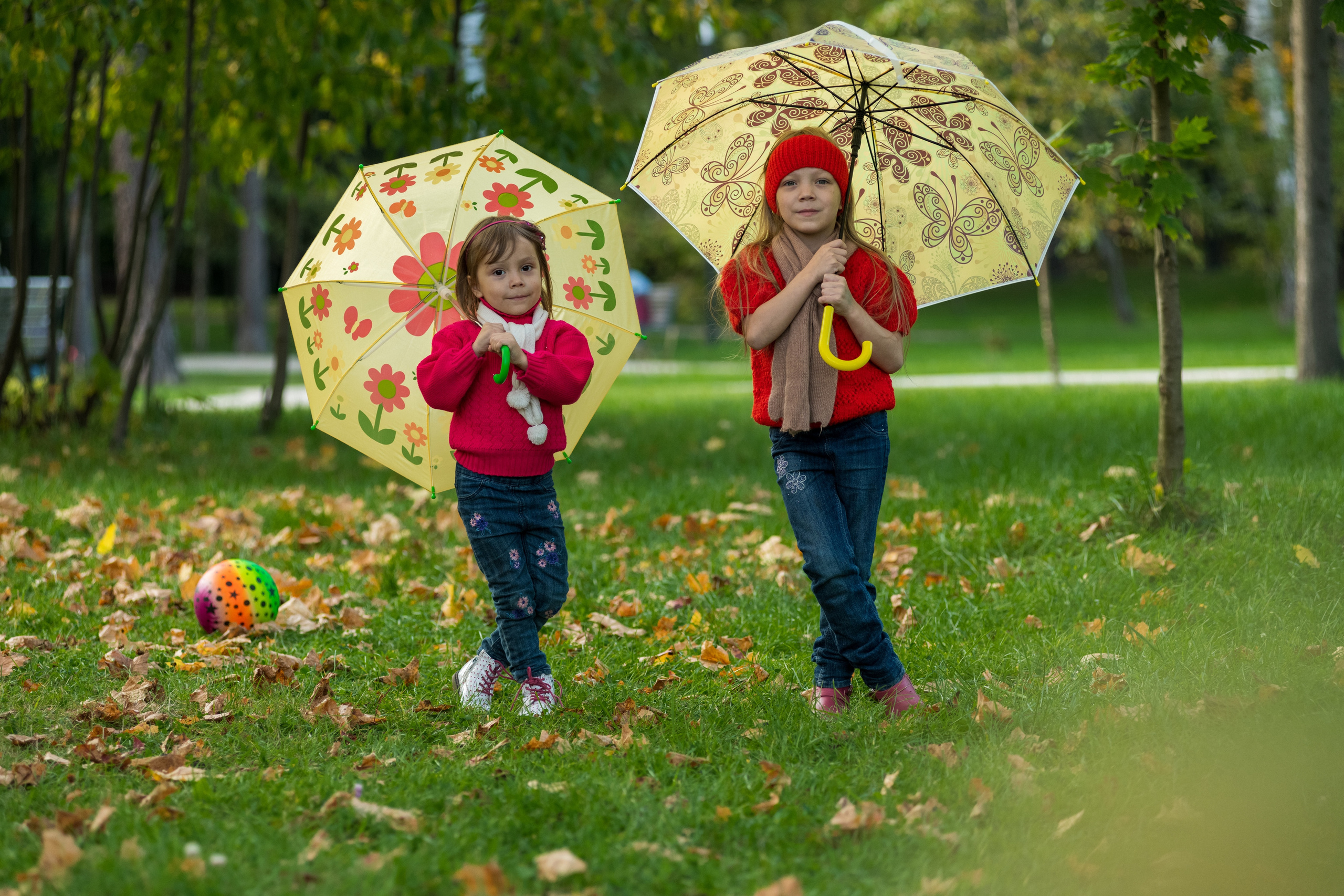Две сестрички стоят в парке на траве с желтыми зонтиками 