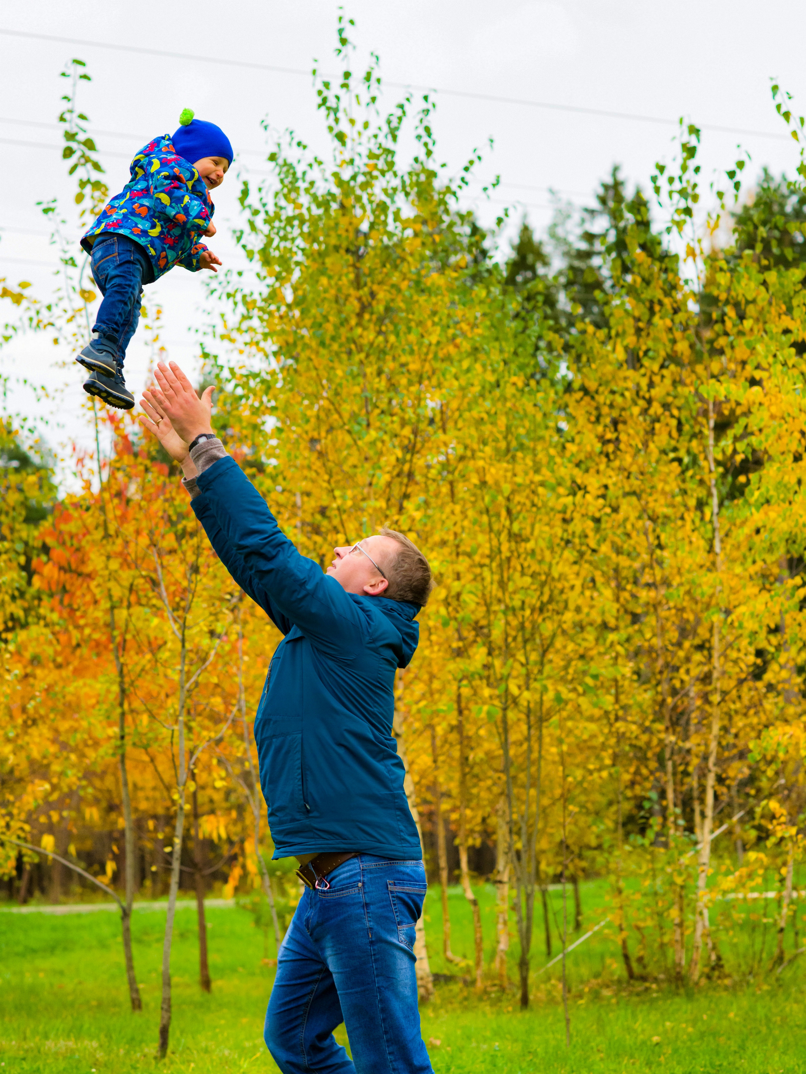 Папа весело играет с ребенком в осеннем парке подкидывает и ловит его