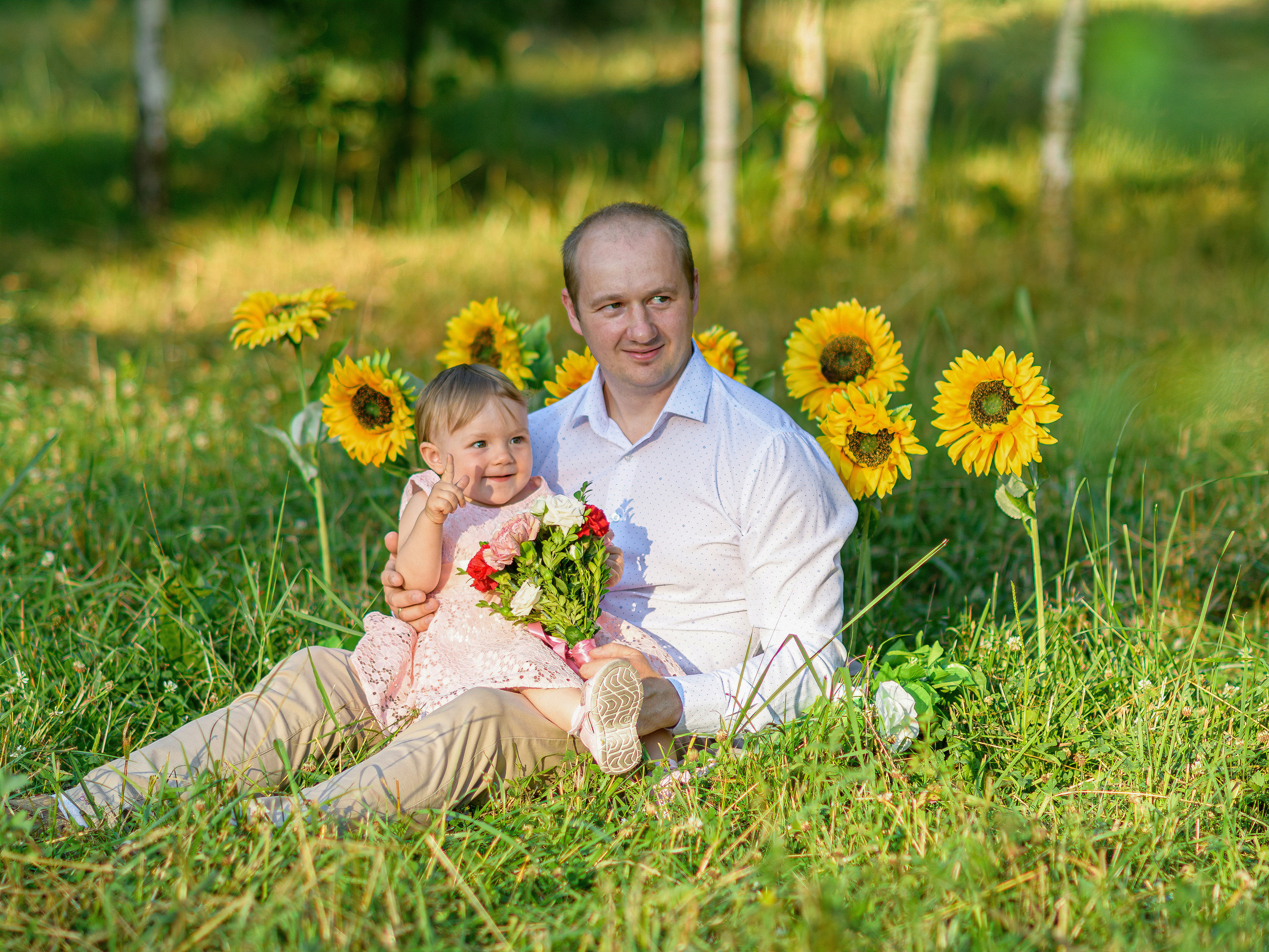 папа сидит на траве в парке с дочкой на руках во круг подсолнухи