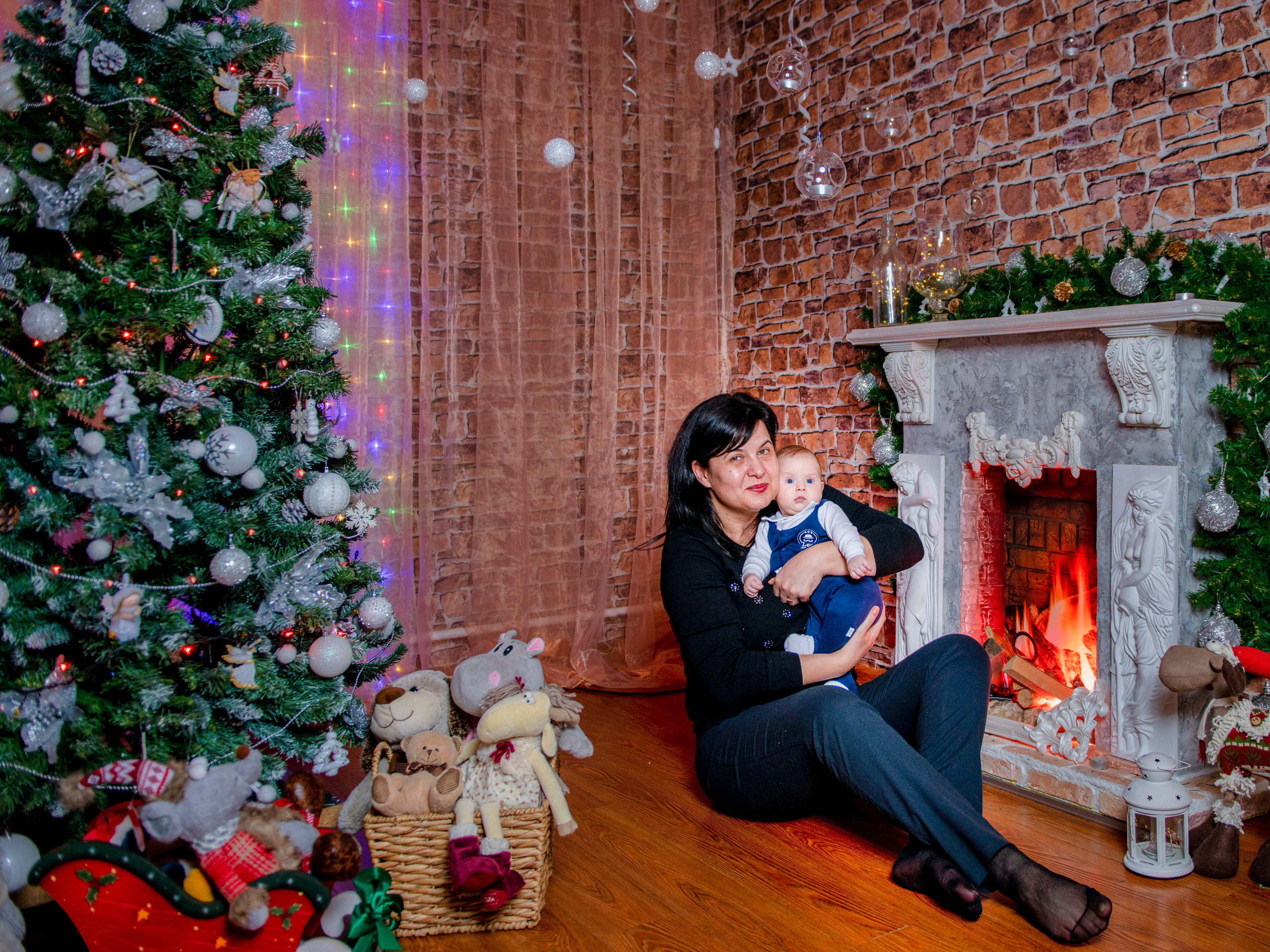 Мама с сыном сидят на полу у камина рядом стоит новогодняя елка