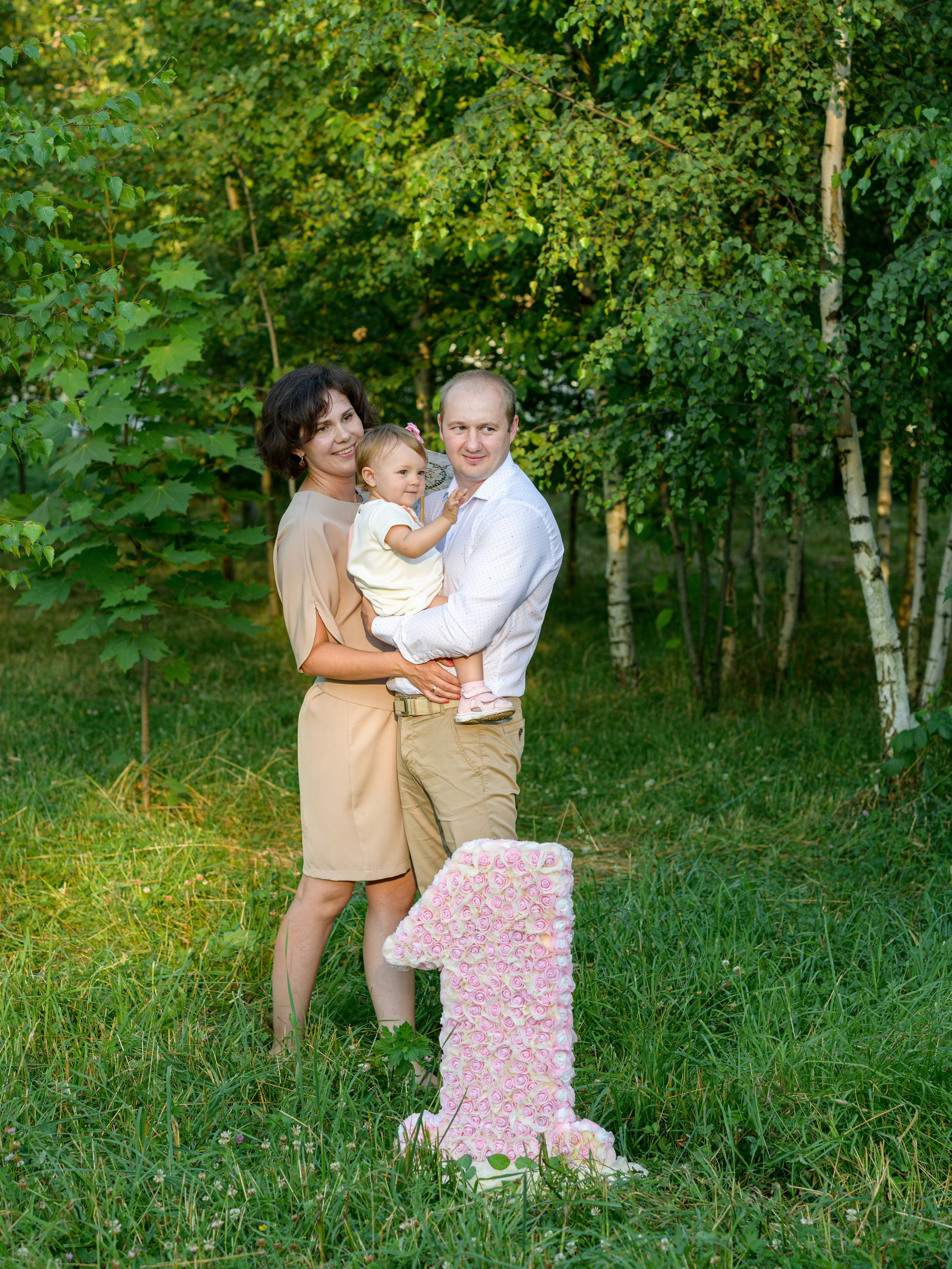 папа с мамой держат на руках дочку на фотосессии в парке