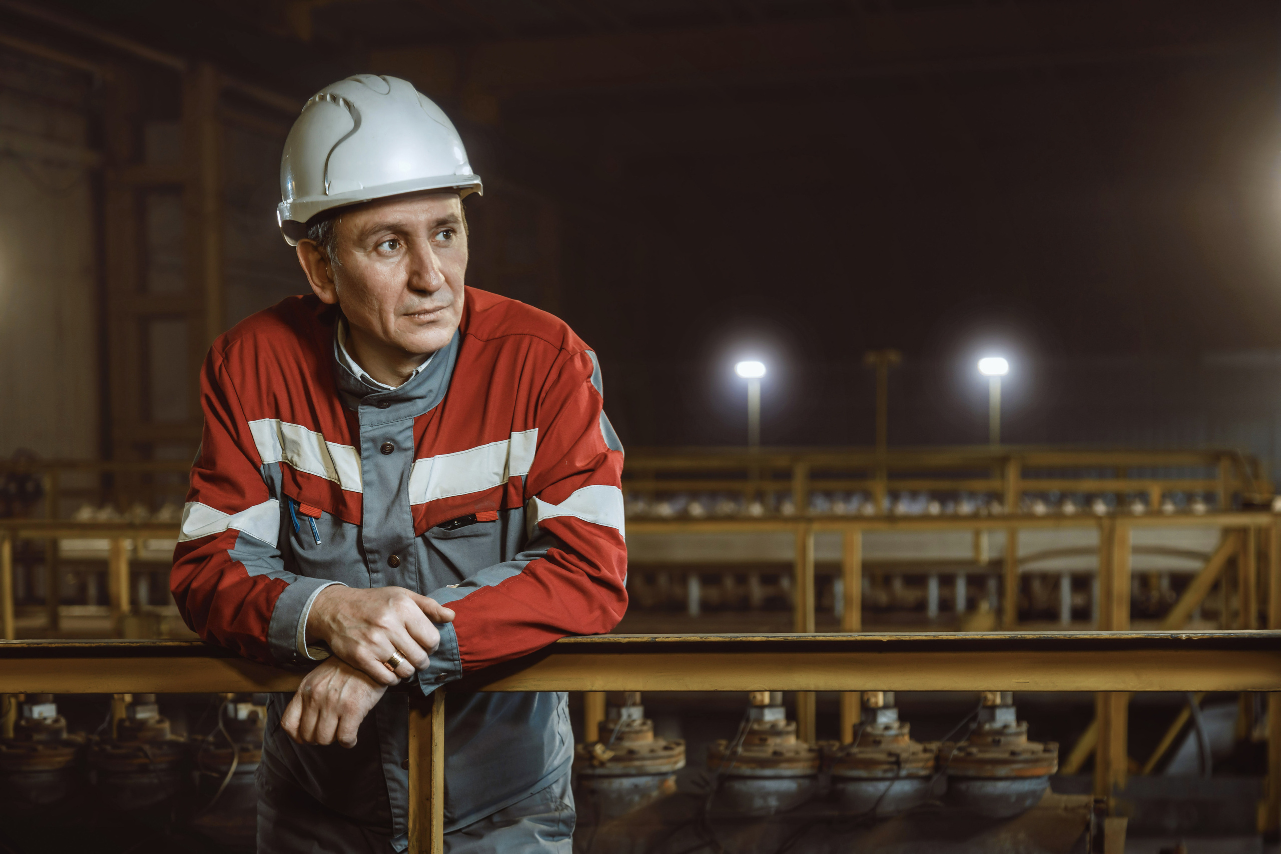 Инженер в белой каске стоит облокотившись на перила