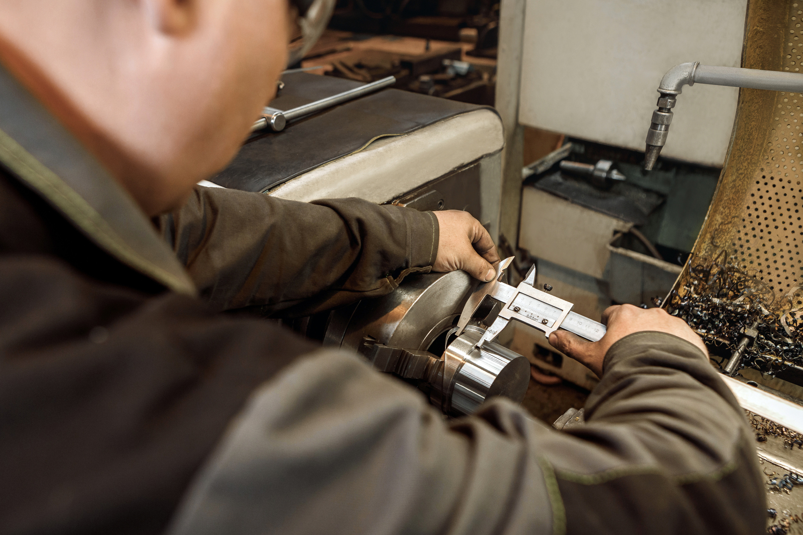 Работник измеряет размер детали после обработки на токарном станке