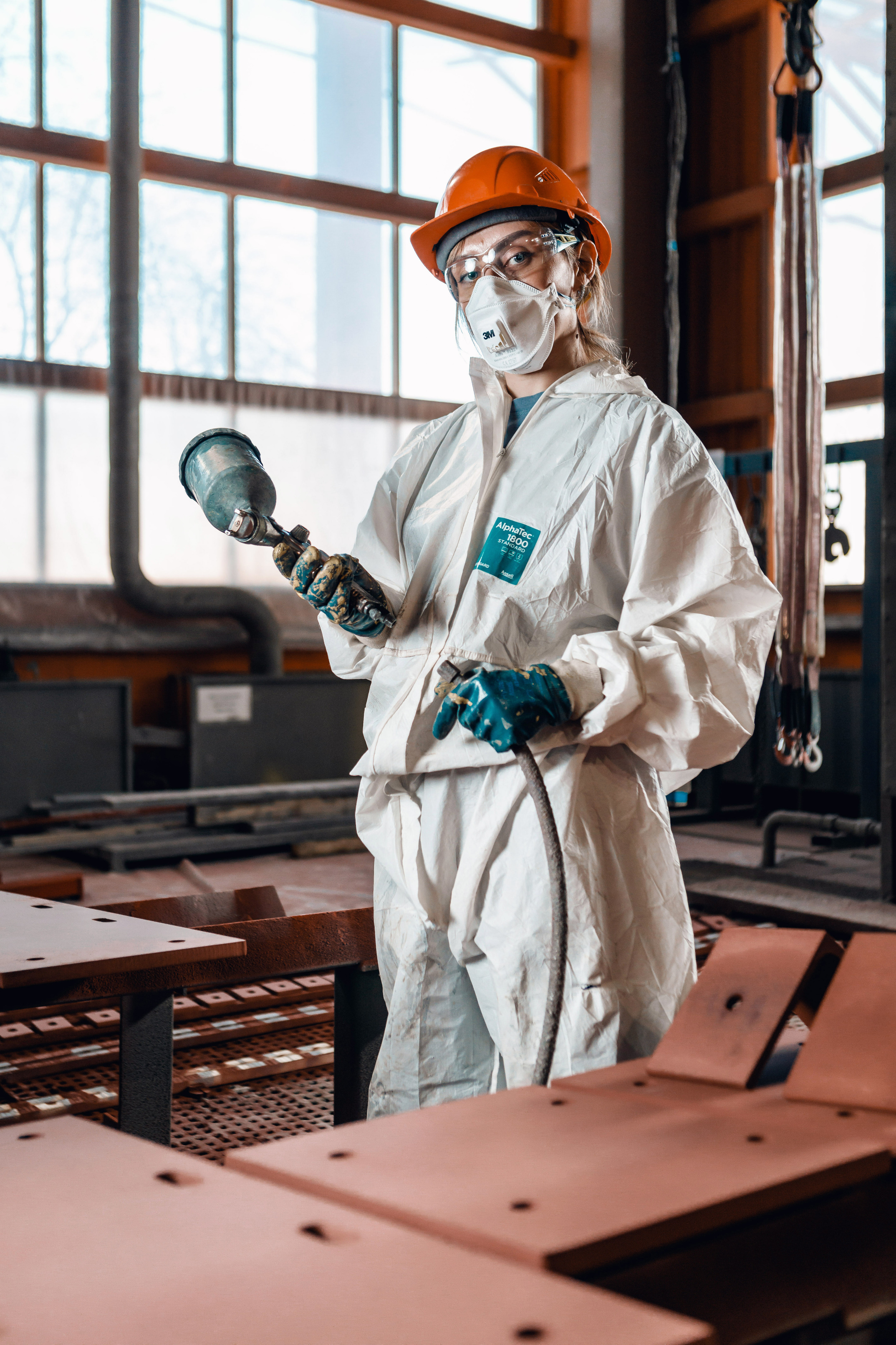 Женщина в защитном костюме и каске с краскопультом в руках