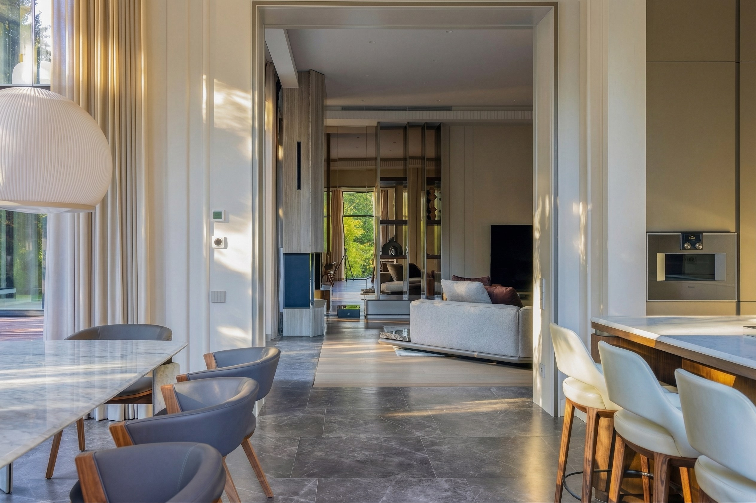 Вид из столовой на гостиную через открытый портал, зонирование пола камнем и деревом, премиальный интерьер дома 1240 м² в Подмосковье, дизайнер Валерия Котович.