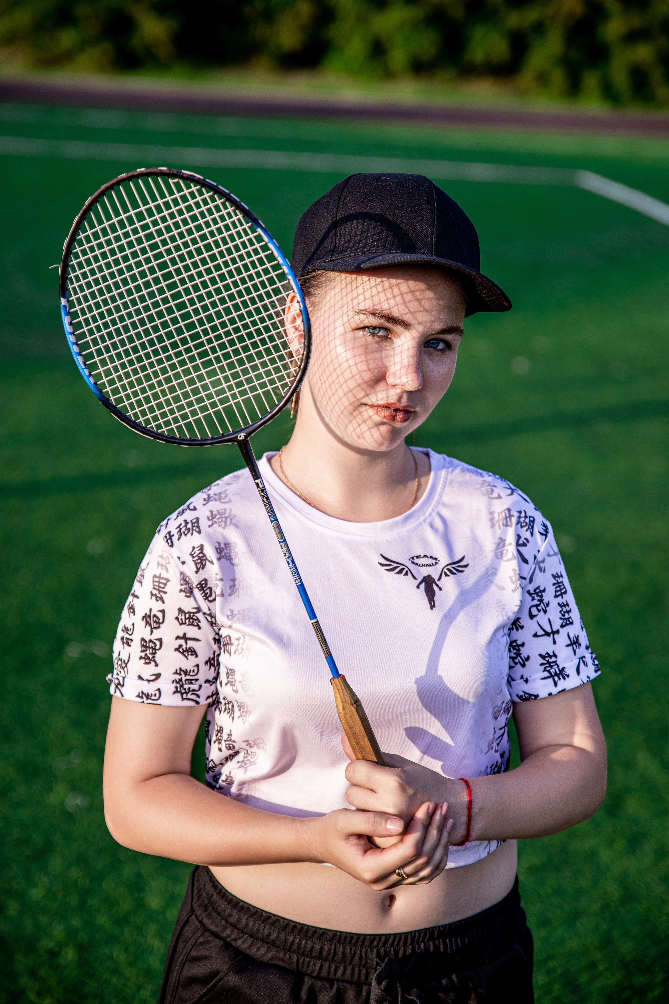 Девушка стоит в белой футболке, с ракеткой от бадминтона