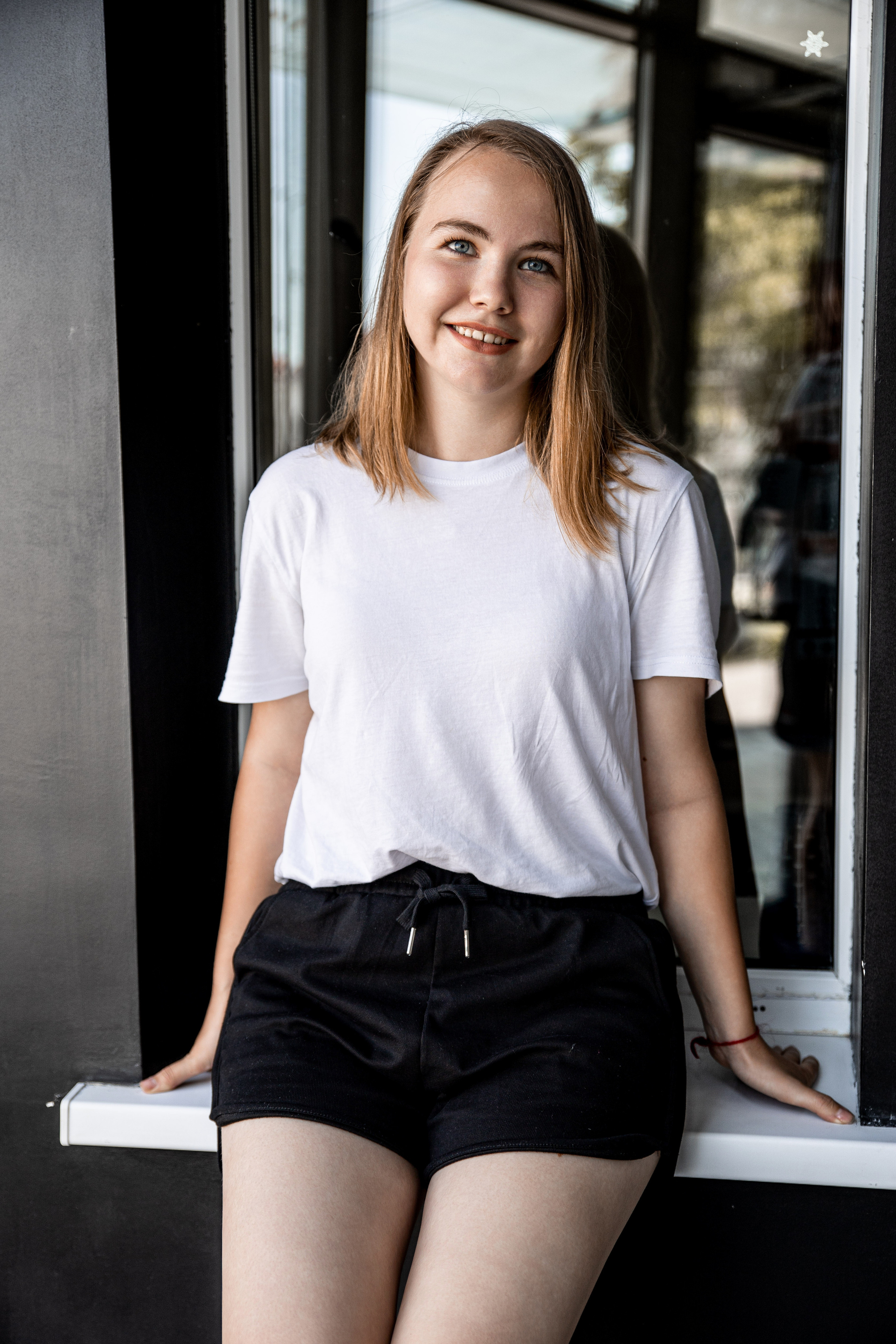 Улыбчивая девушка в интерьере на чёрном фоне, в белой футболке, в шортах