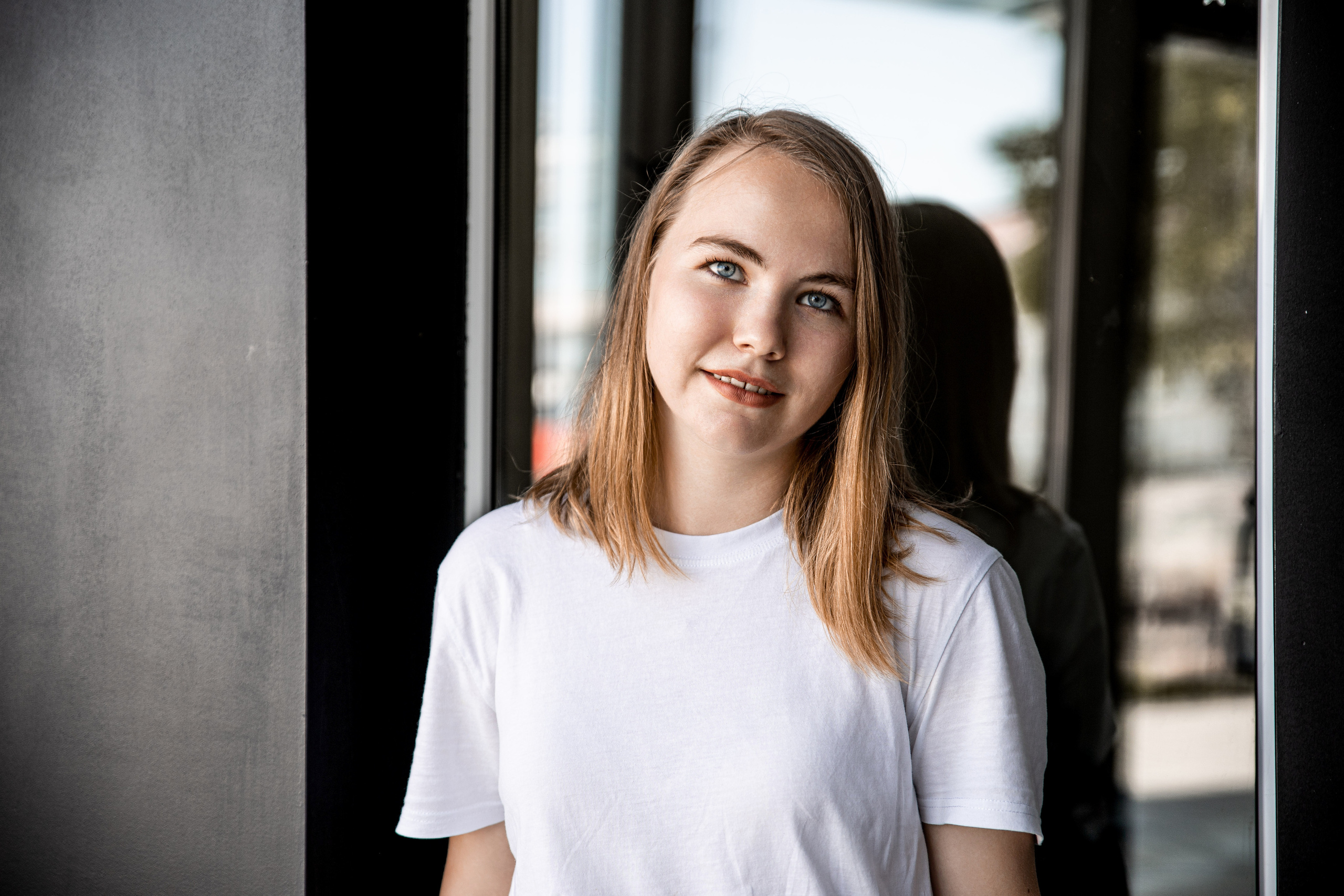 Девушка на фоне зеркального окна, в белой футболке, чёрные стены