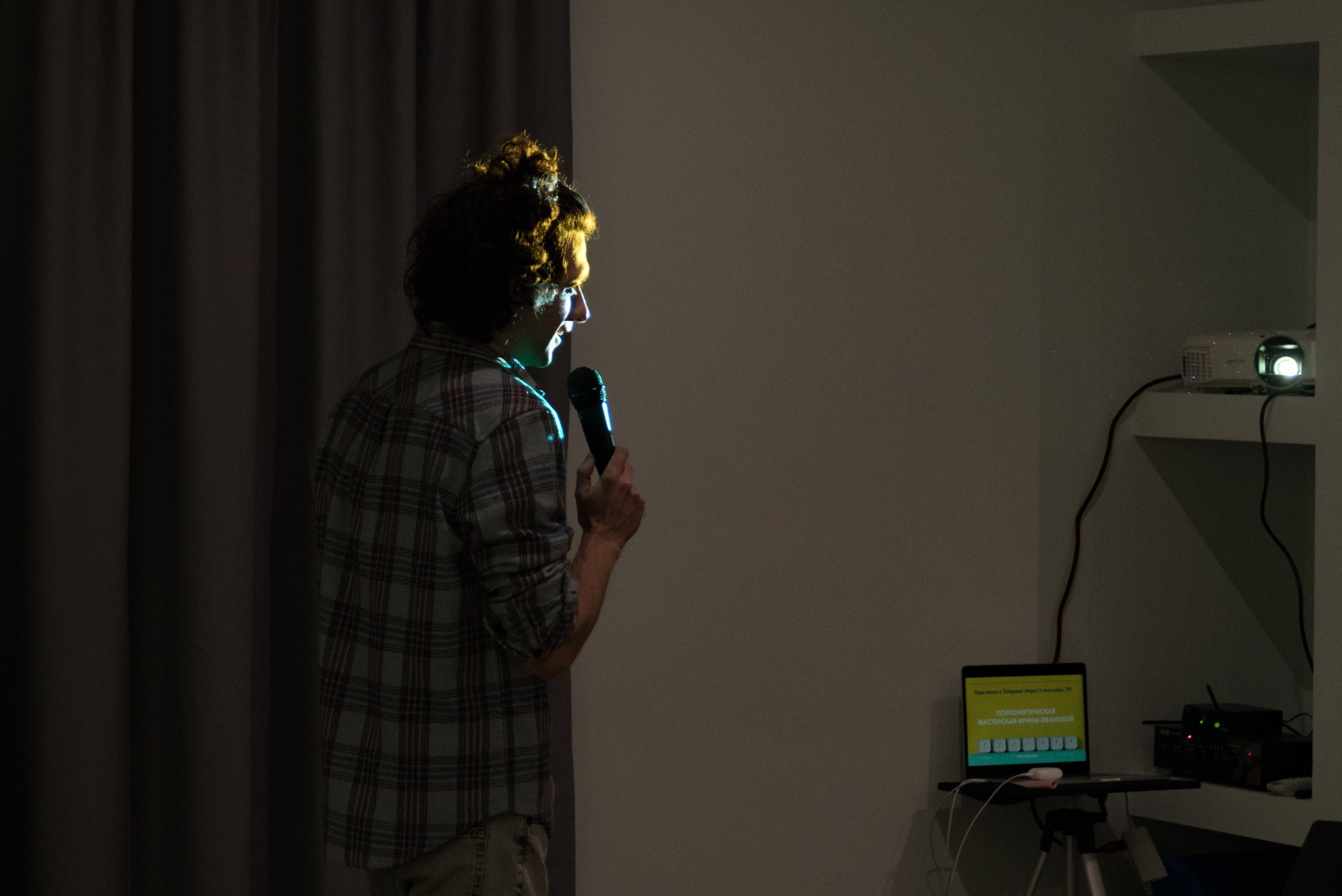 Мужчина проверяет микрофон. Темнота, освещён только его силуэт, на заднем плане экран ноутбука.
