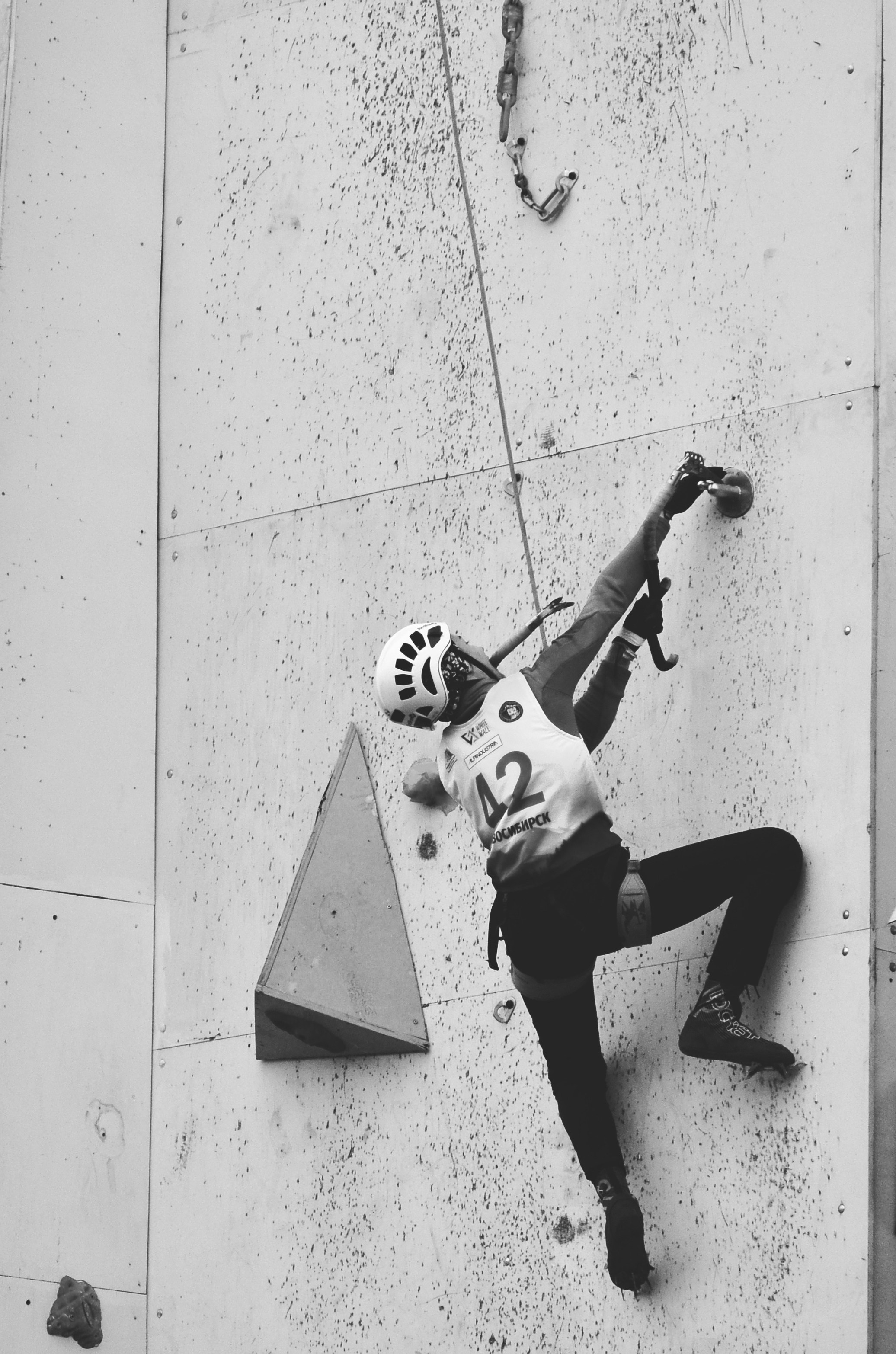 На этой фотографии запечатлен момент спортивного ледолазания. Спортсмен поднимается по ледяной стене, демонстрируя невероятную силу и ловкость. Ледолазание — это экстремальный вид спорта, требующий отличной физической подготовки и навыков альпинизма. Вертикальный подъем по ледяной поверхности требует не только физической силы, но и умения правильно распределять вес и находить надежные точки опоры.