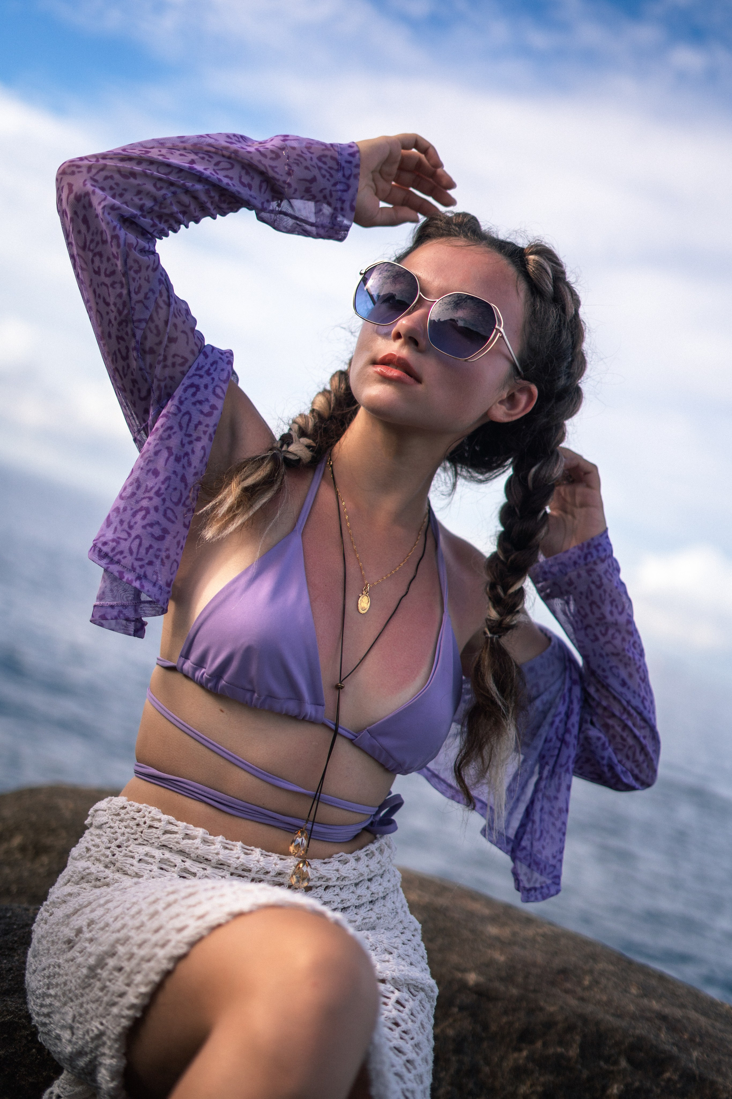a young beauty in a purple swimsuit on the rocks at the ocean's edge