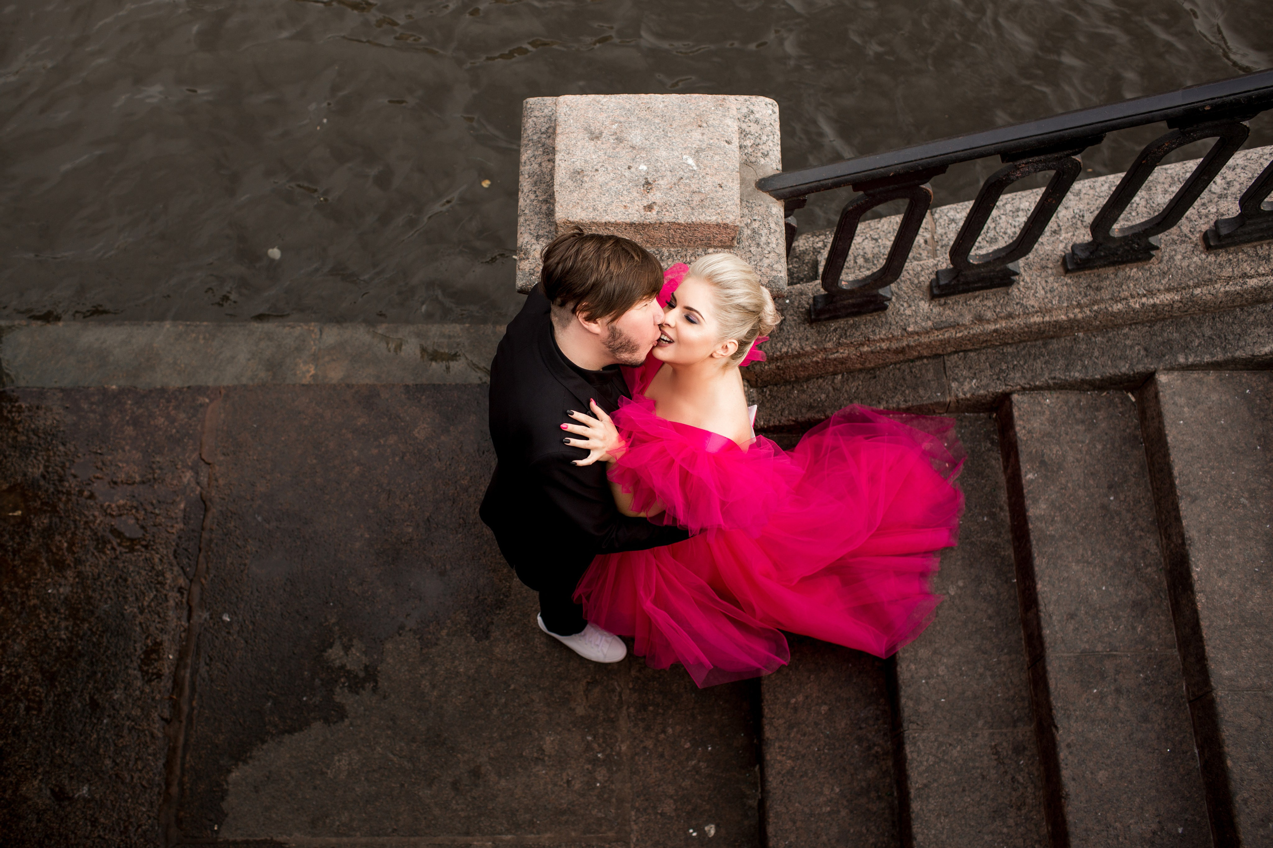 Свадебная пара улыбается в лучах солнца, невеста в эффектном красном наряде