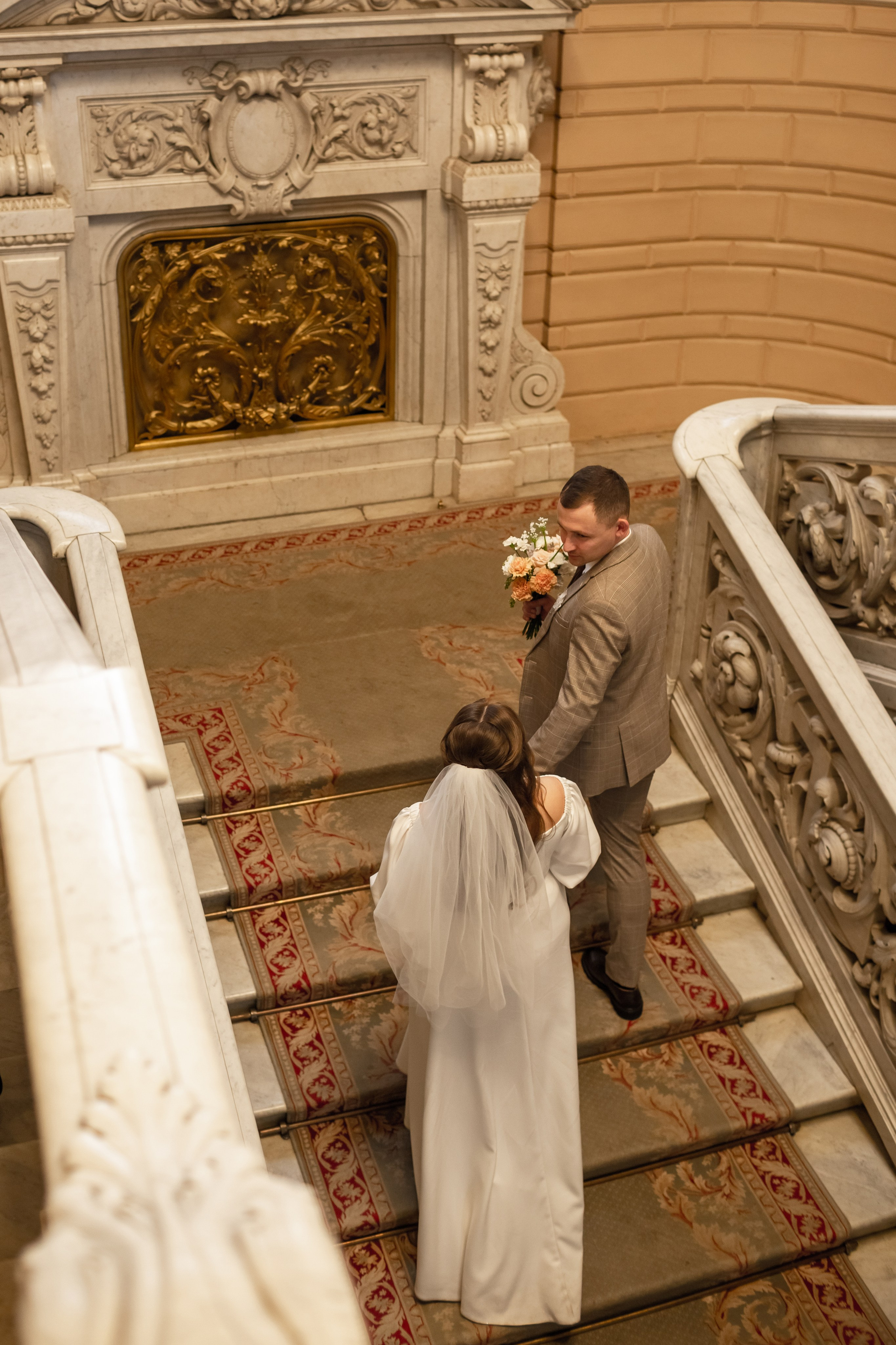 Жених и невеста поднимаются по красивой лестнице во дворце бракосочетания.