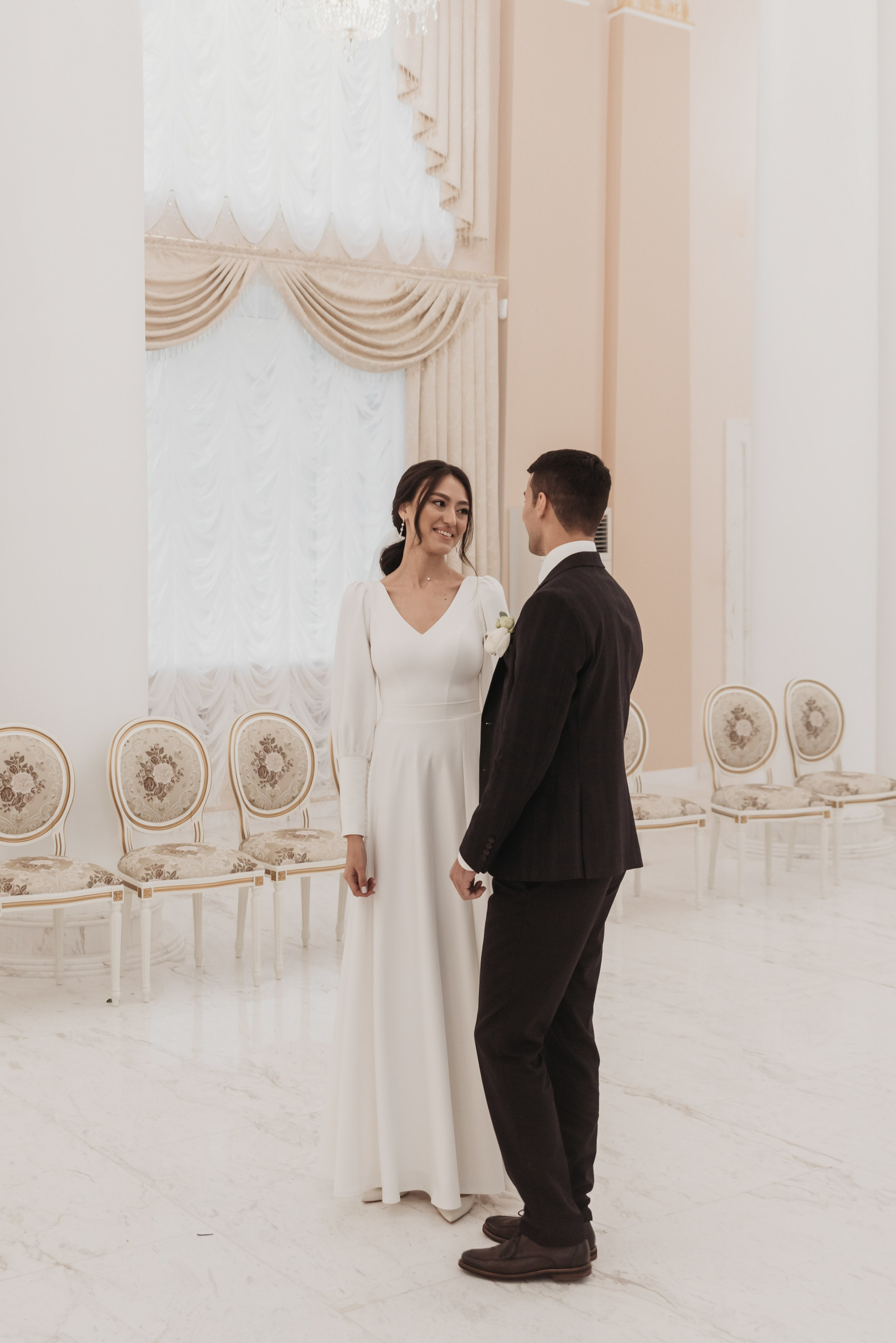 Счастливая пара, нежно обнимающаяся и смотрящая друг на друга в момент любви. Невеста в белом платье и фате, жених в стильном костюме. Идеальная фотография для свадебного альбома, отражающая эмоции и близость в их важный день