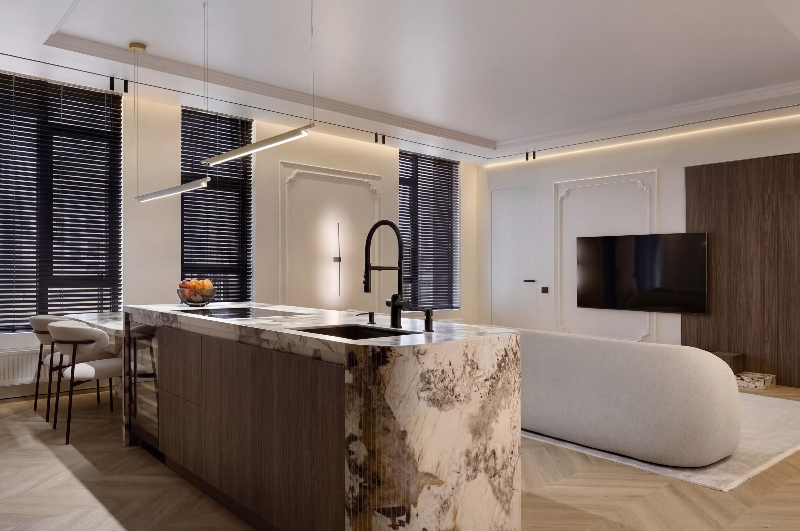 Интерьер кухни-гостиной в квартире 120 м² от дизайнера Валерии Котович: кухонный остров из мрамора, минималистичный диван-«облако» и классические молдинги на стенах в теплом освещении.
