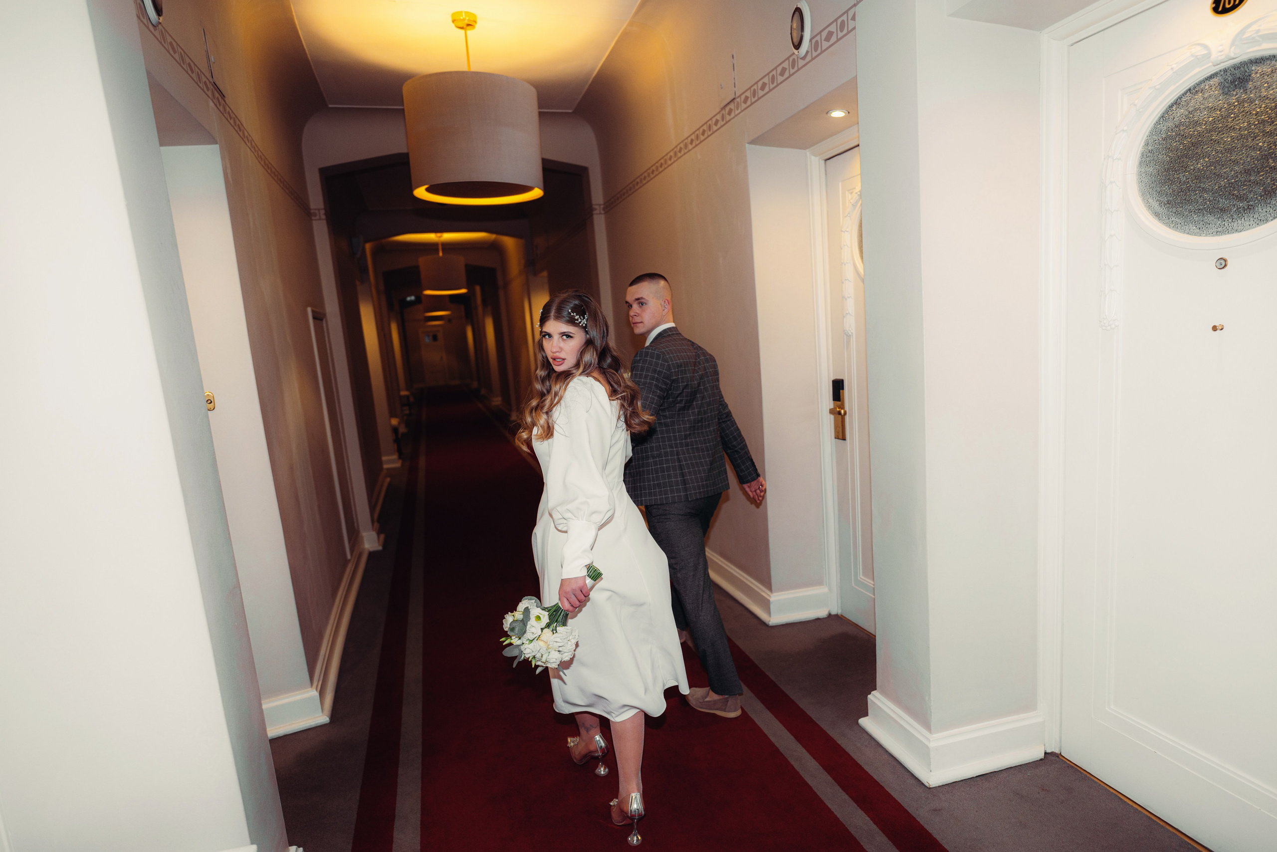 Жених держит за руку невесту и бежит с ней по коридору гостиницы астория