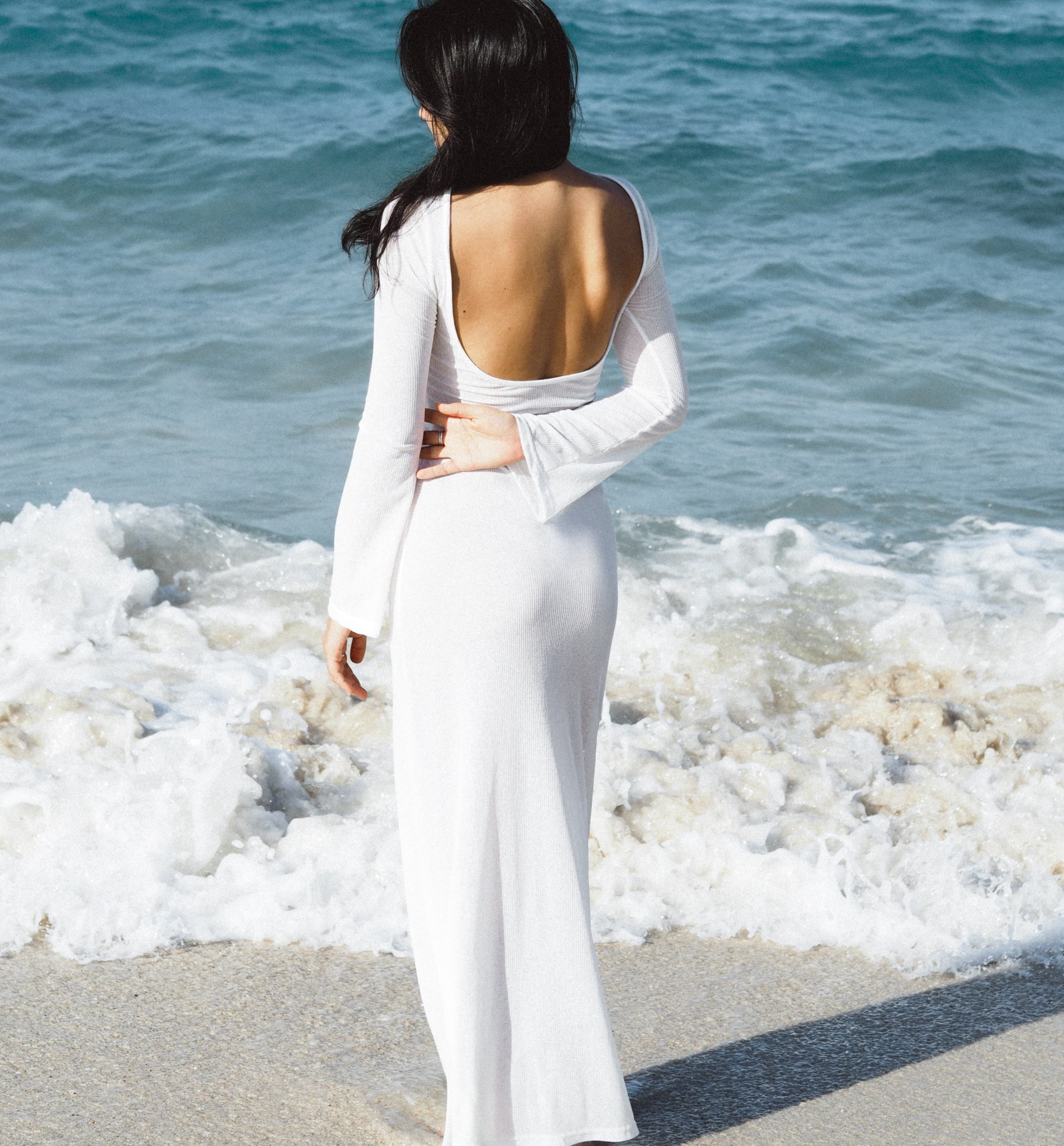 Девушка в платье с открытой спиной фотографируется и позирует на море.