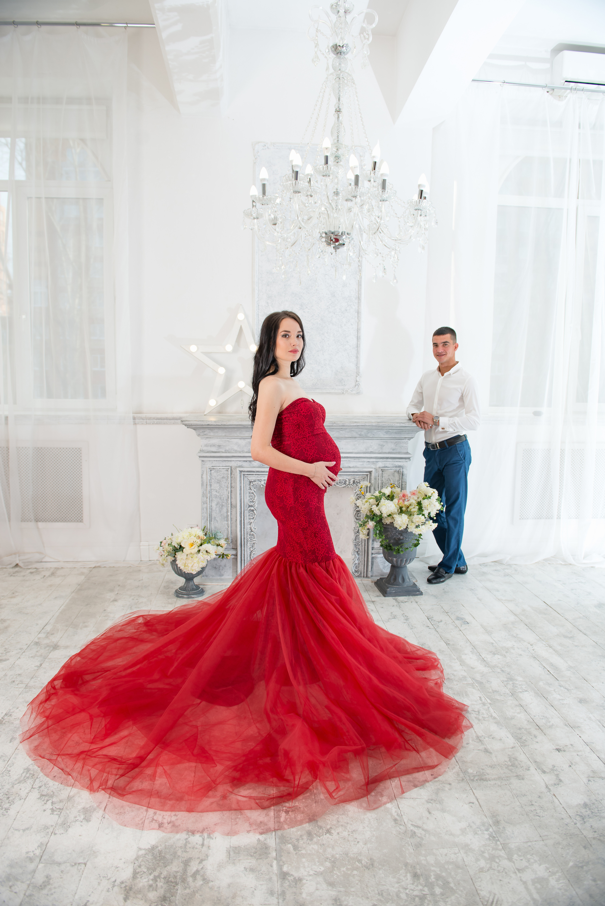 Беременная девушка в красном платье-рыбке со шлейфом на фотосессии в фотостудии