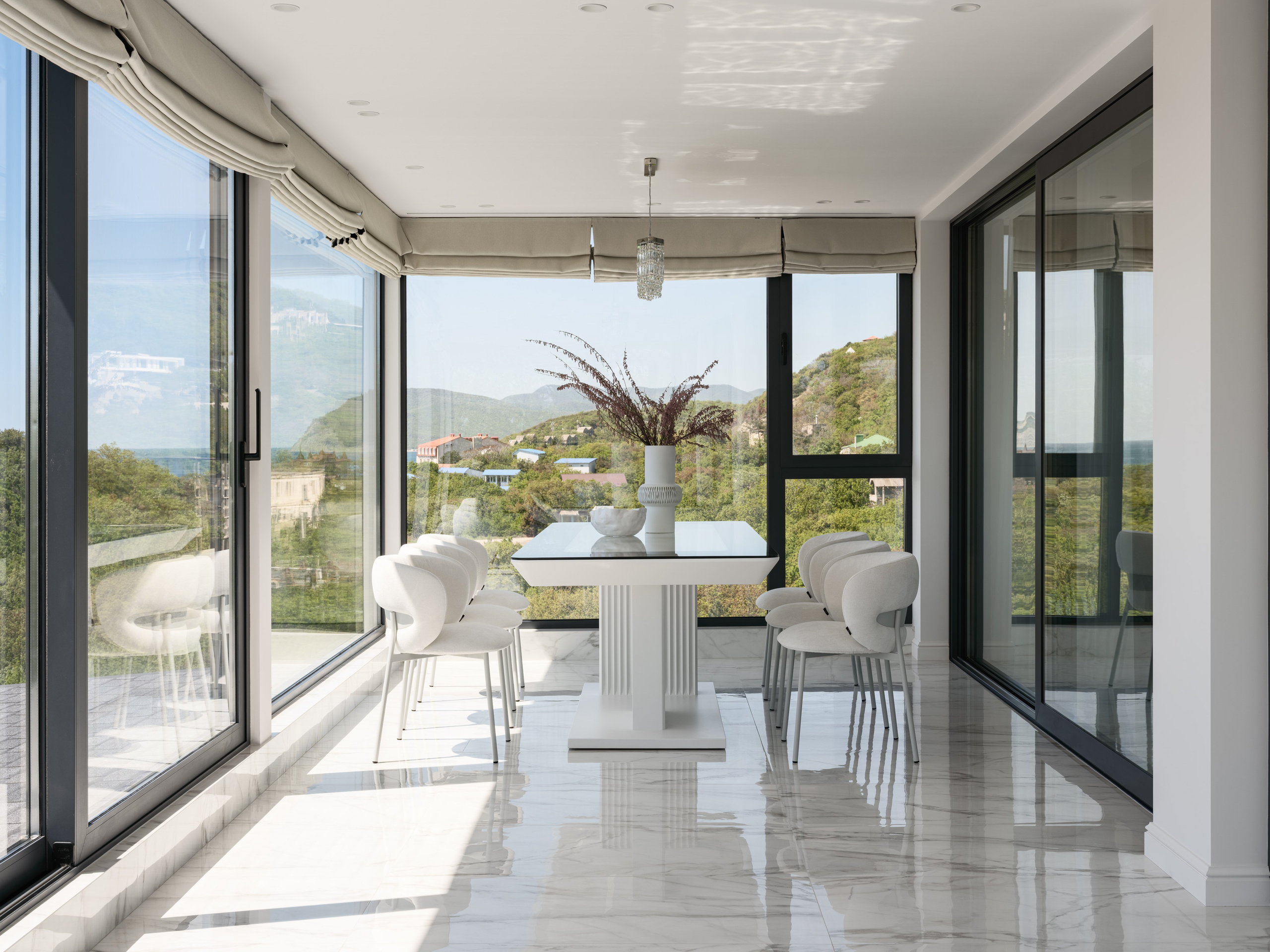 Элегантная столовая зона с панорамным остеклением и видом на горы, белым столом и мягкими стульями на глянцевом мраморном полу — светлый интерьер, созданный дизайнером Алёной Боярской при участии стилиста Натальи Якушевой, фото Сергея Денисенко.