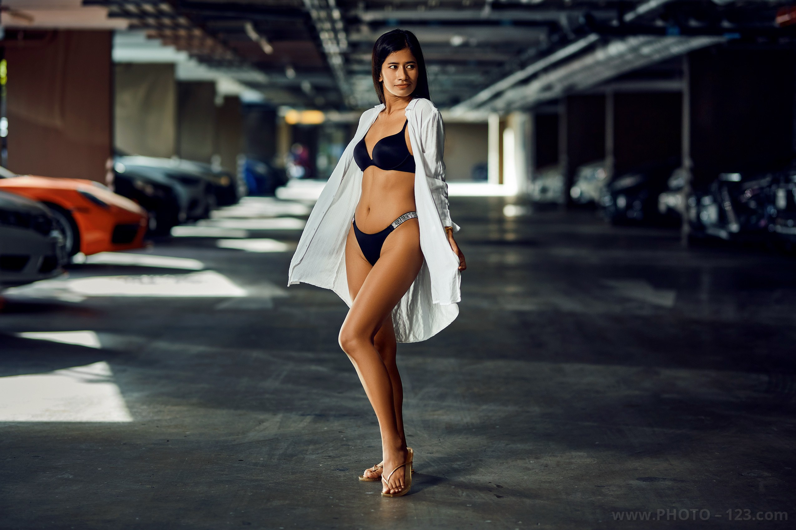 Fashion portrait of a woman in black lingerie and white shirt walking through an underground parking garage
