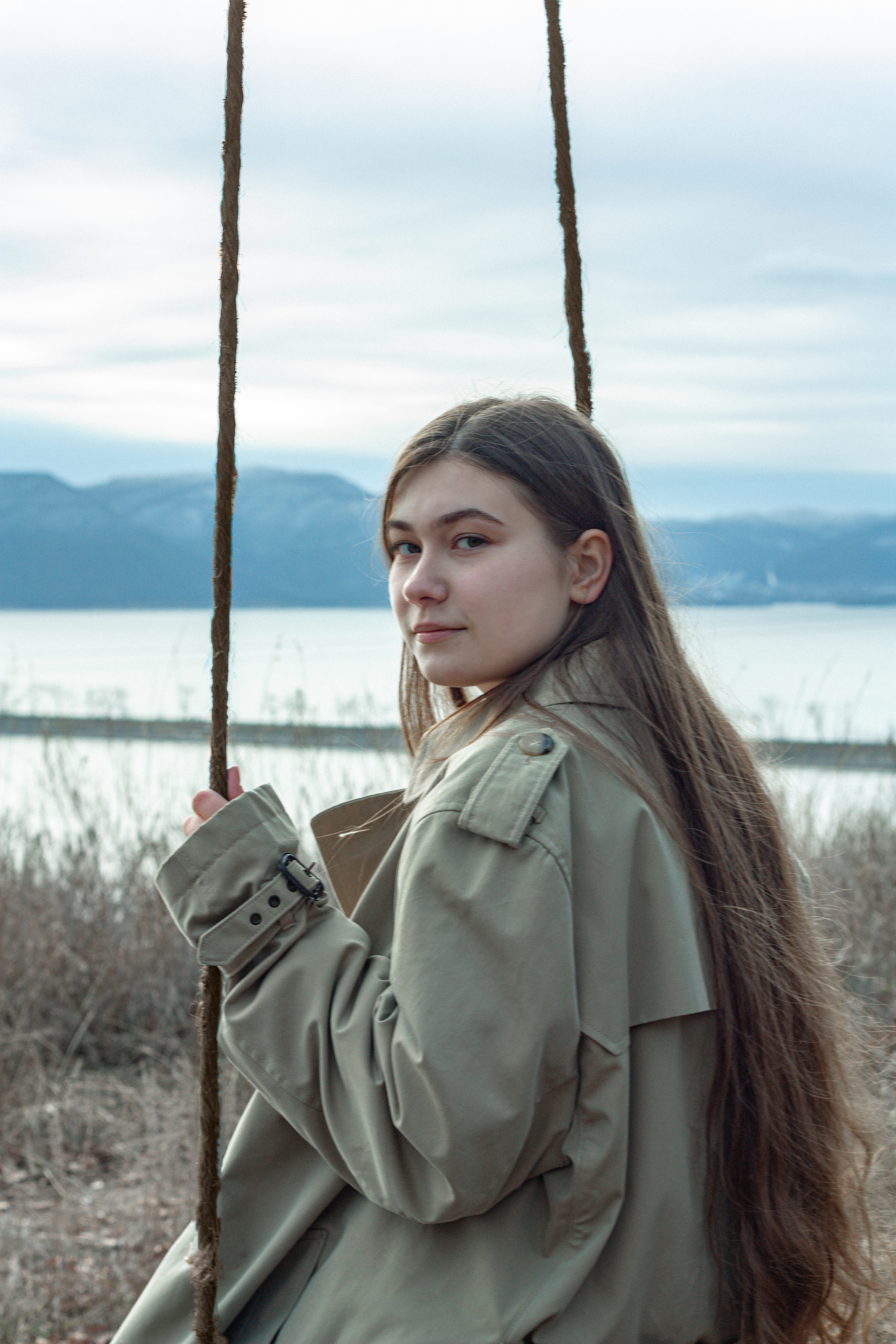 Девушка сидит на подвесных качелях в лесу на фоне гор. 