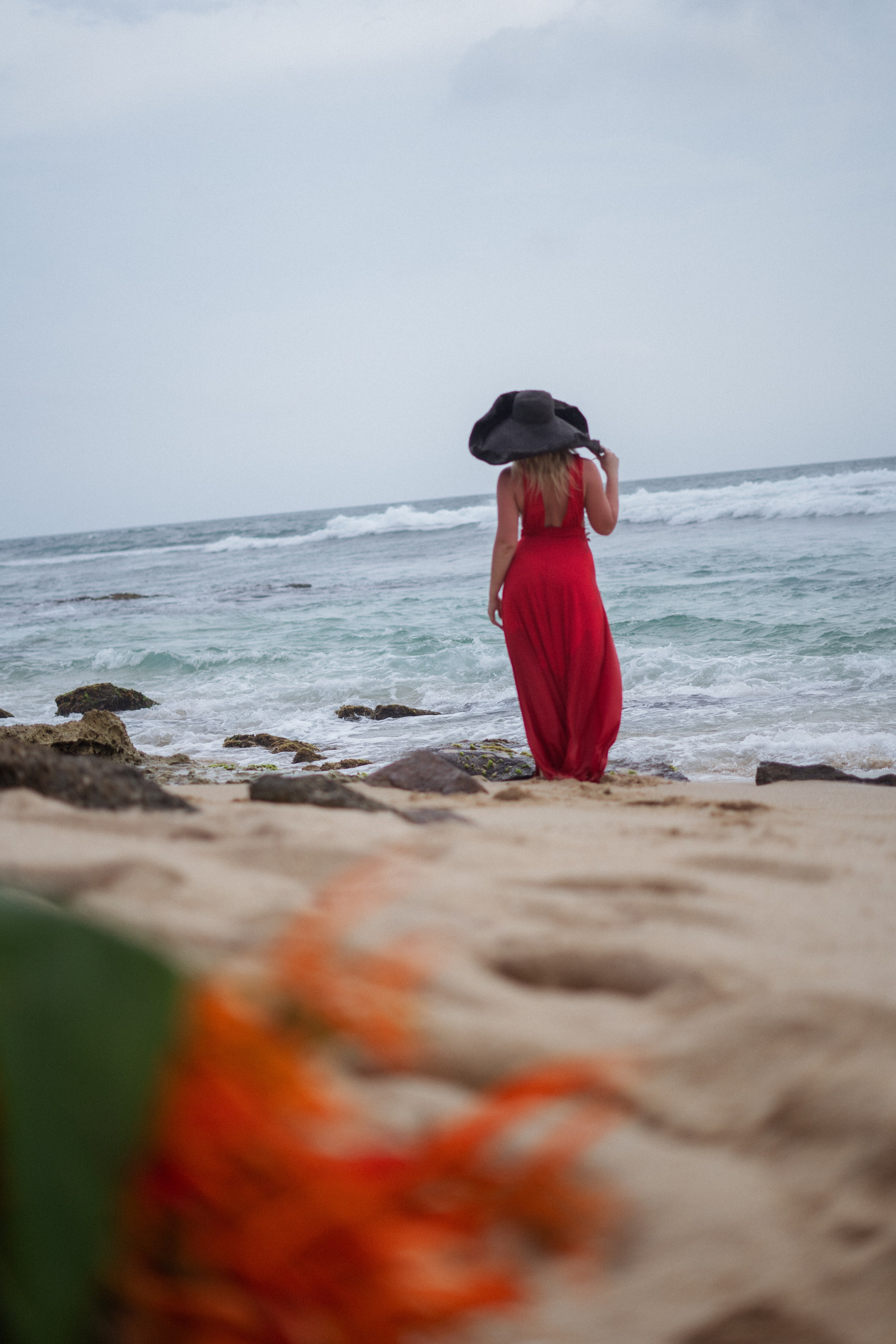 a blonde in a red dress with the ocean waves in the background