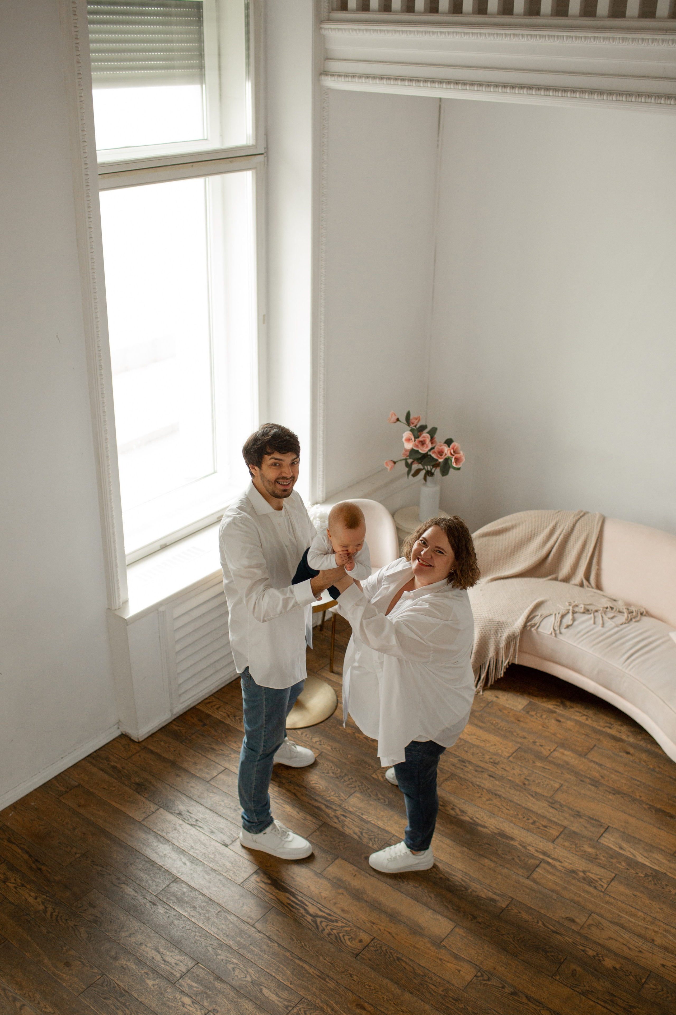 Счастливые родители танцуют с малышом на руках в фотостудии.