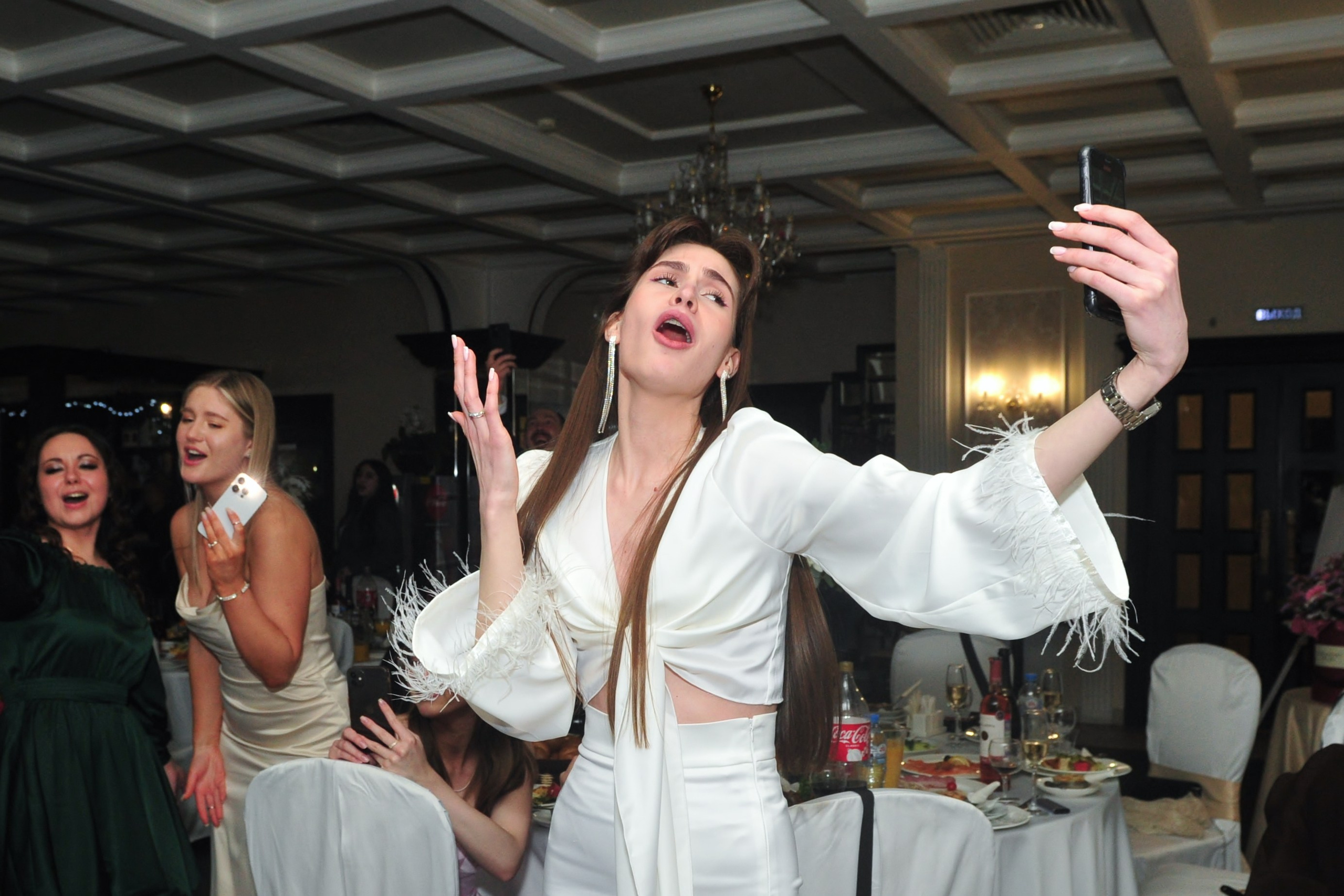 Девушка танцует, поет и делает селфи на свадебном банкете в ресторане