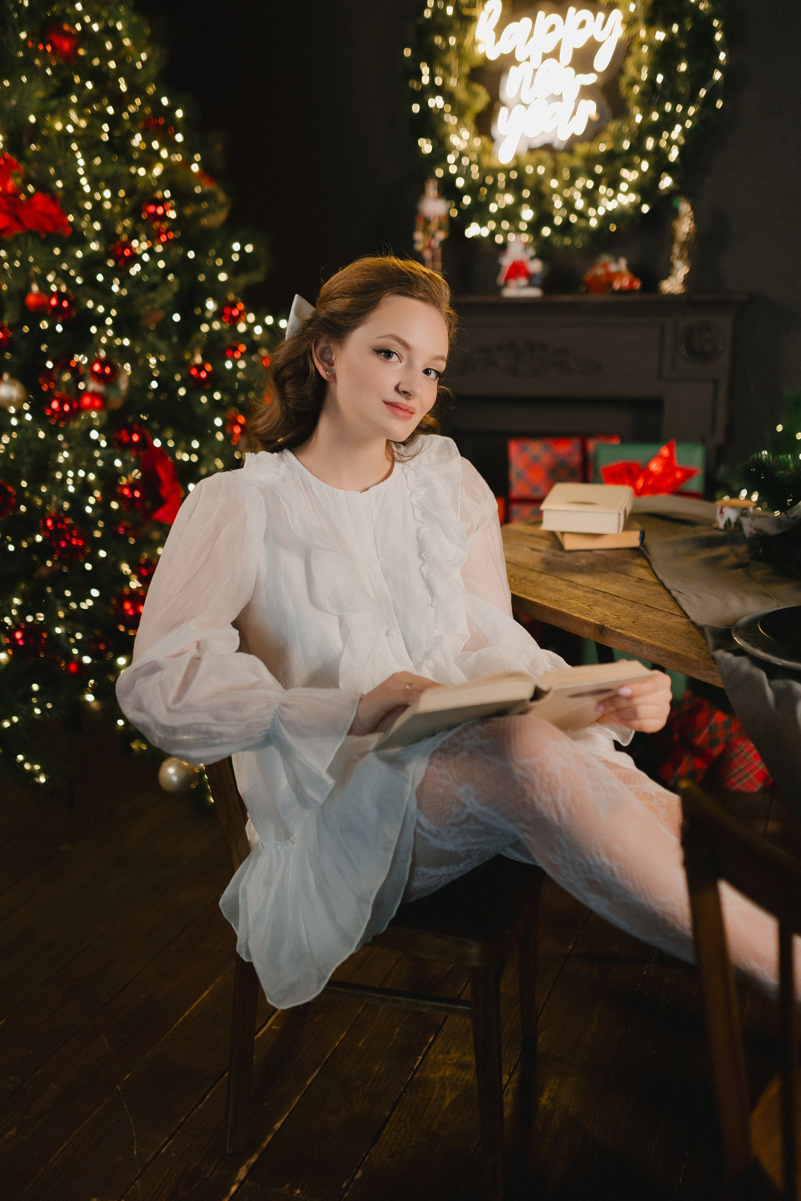 Девушка сидит на диване перед камином, держа чашечку горячего какао или чая в руках.