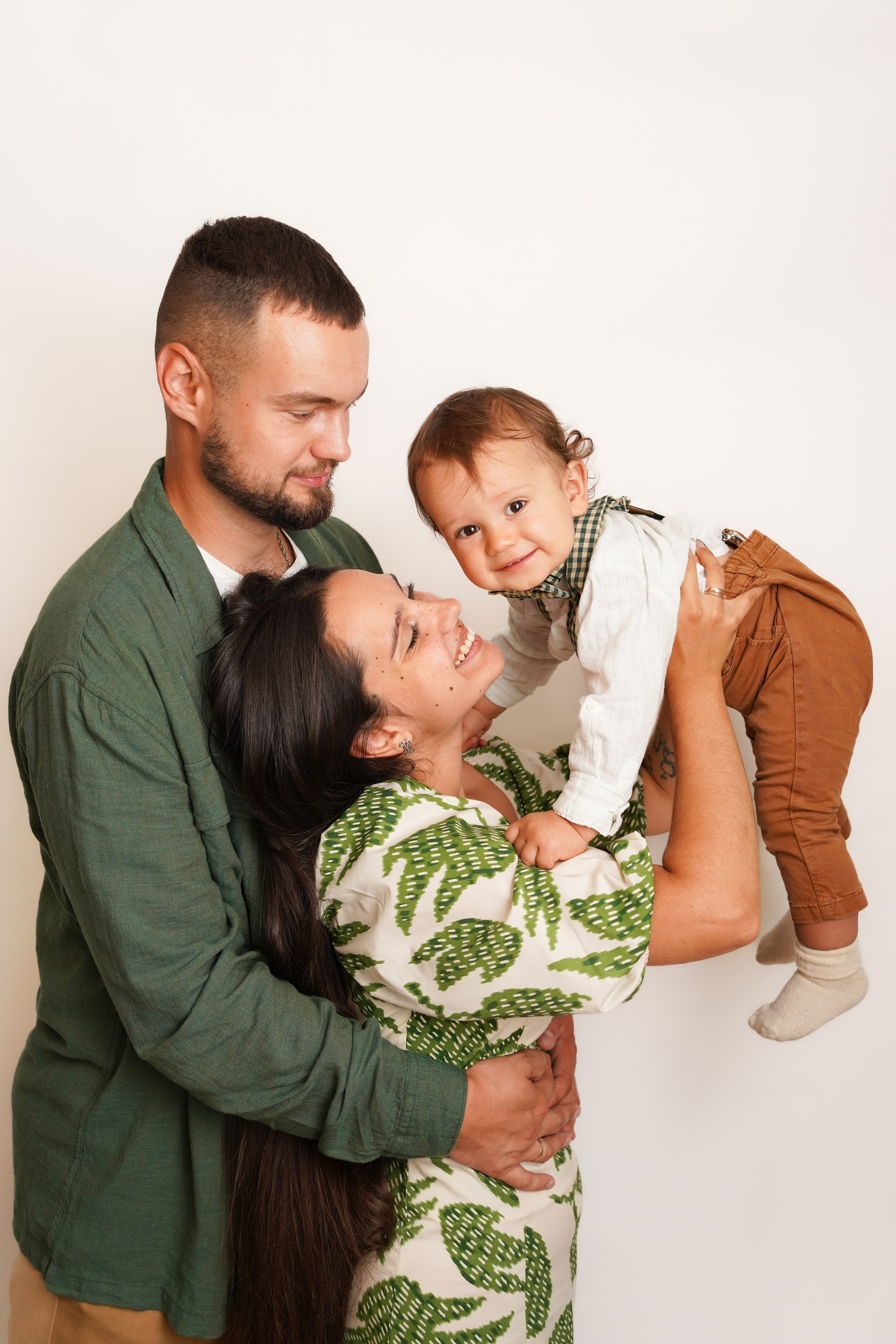  На фото мама поднимает вверх малыша. Папа смотрит на сына и улыбается.