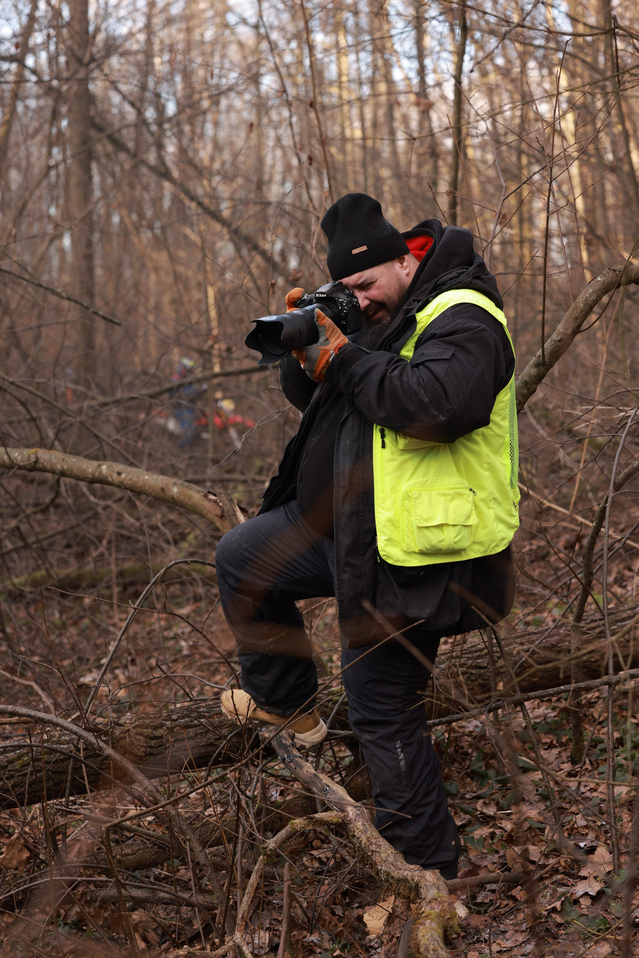 фотограф в яркой жилетке снимает мото соревнования эндуро в лесу осенью