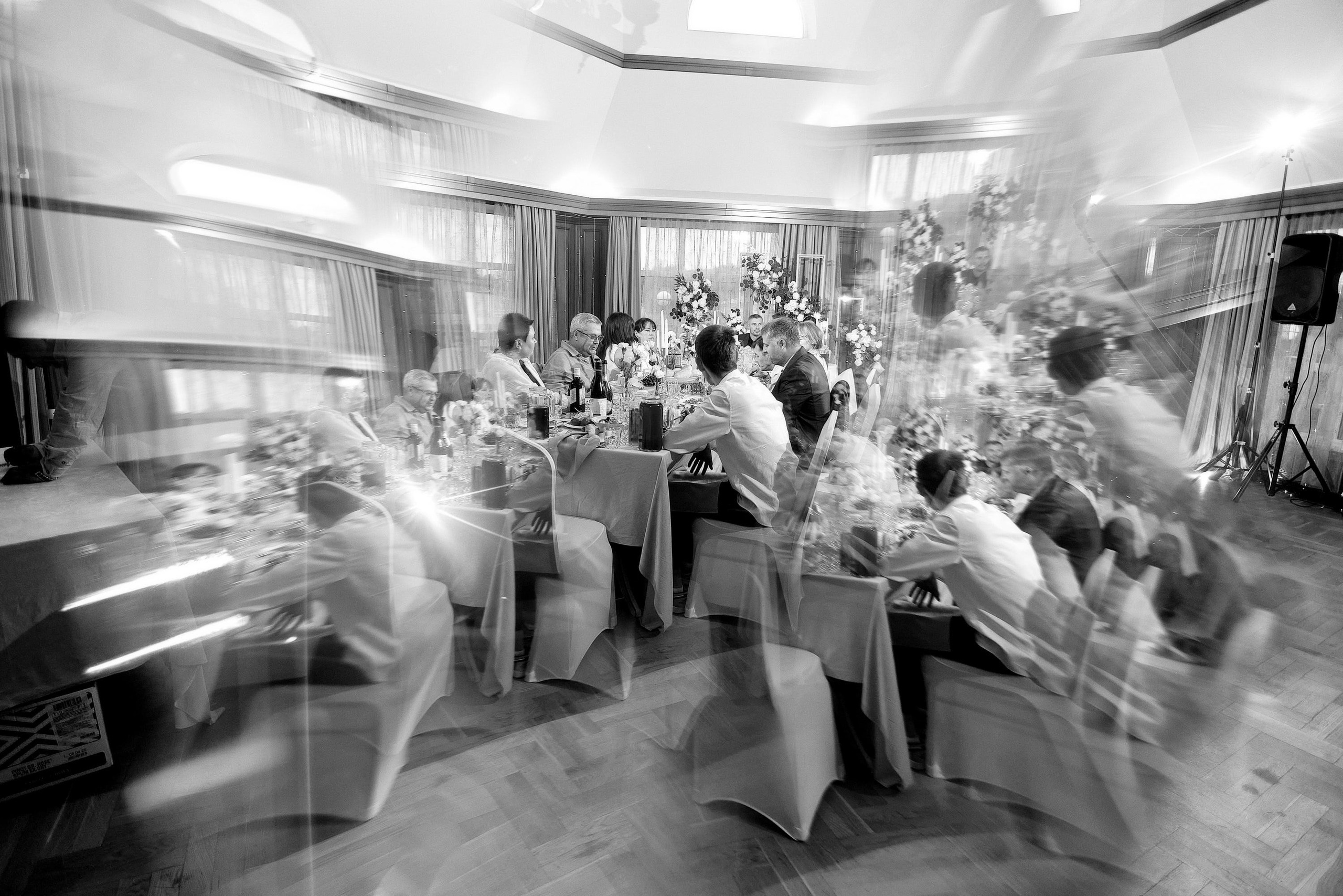 Свадебный банкет за длинным столом, гости в движении, художественный чёрно-белый эффект смаза