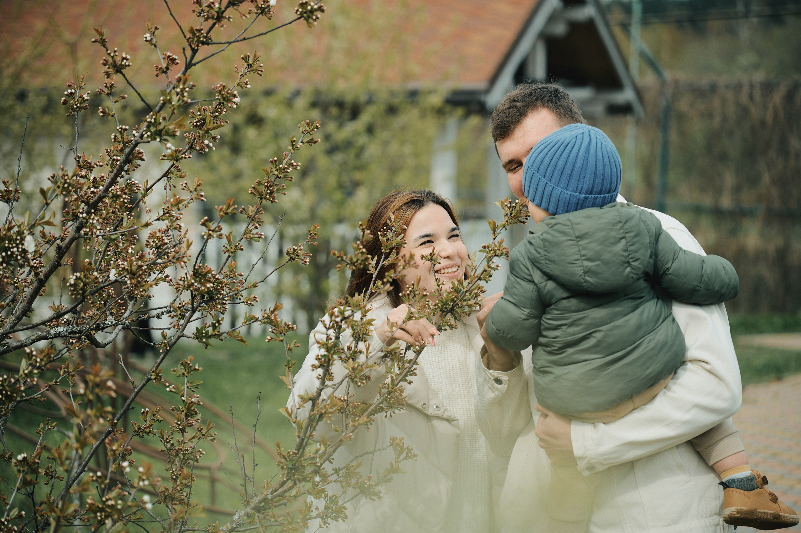 семья у цветущего куста, ребёнок на руках у папы, мама улыбается