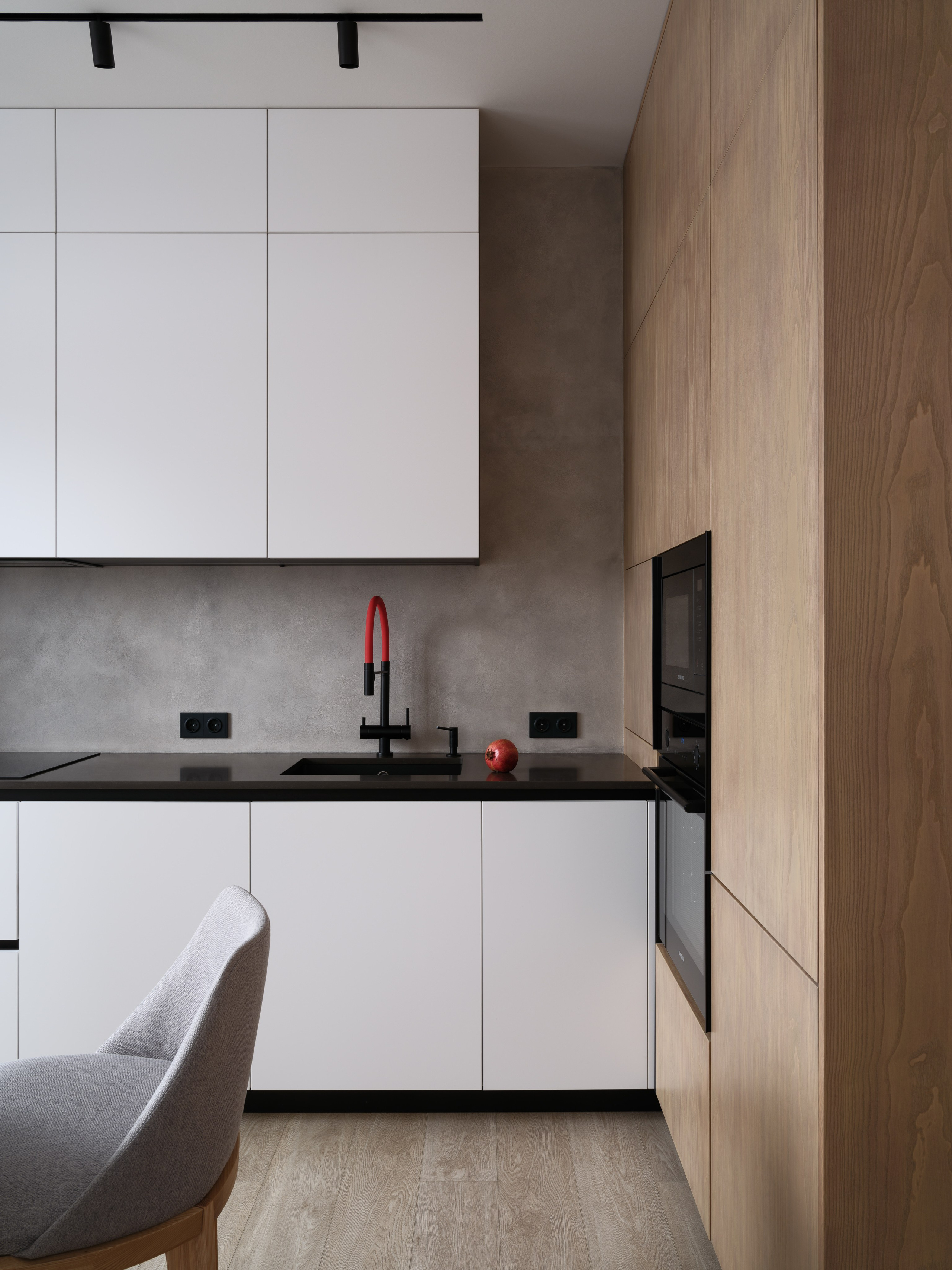 Современная кухня в минималистичном стиле с деревянными фасадами, белыми шкафами, черной столешницей и обеденной зоной с круглым столом и дизайнерскими стульями. Автор проекта — дизайнеры Евгения Княжева и Владлена Привалова, фотограф Сергей Денисенко