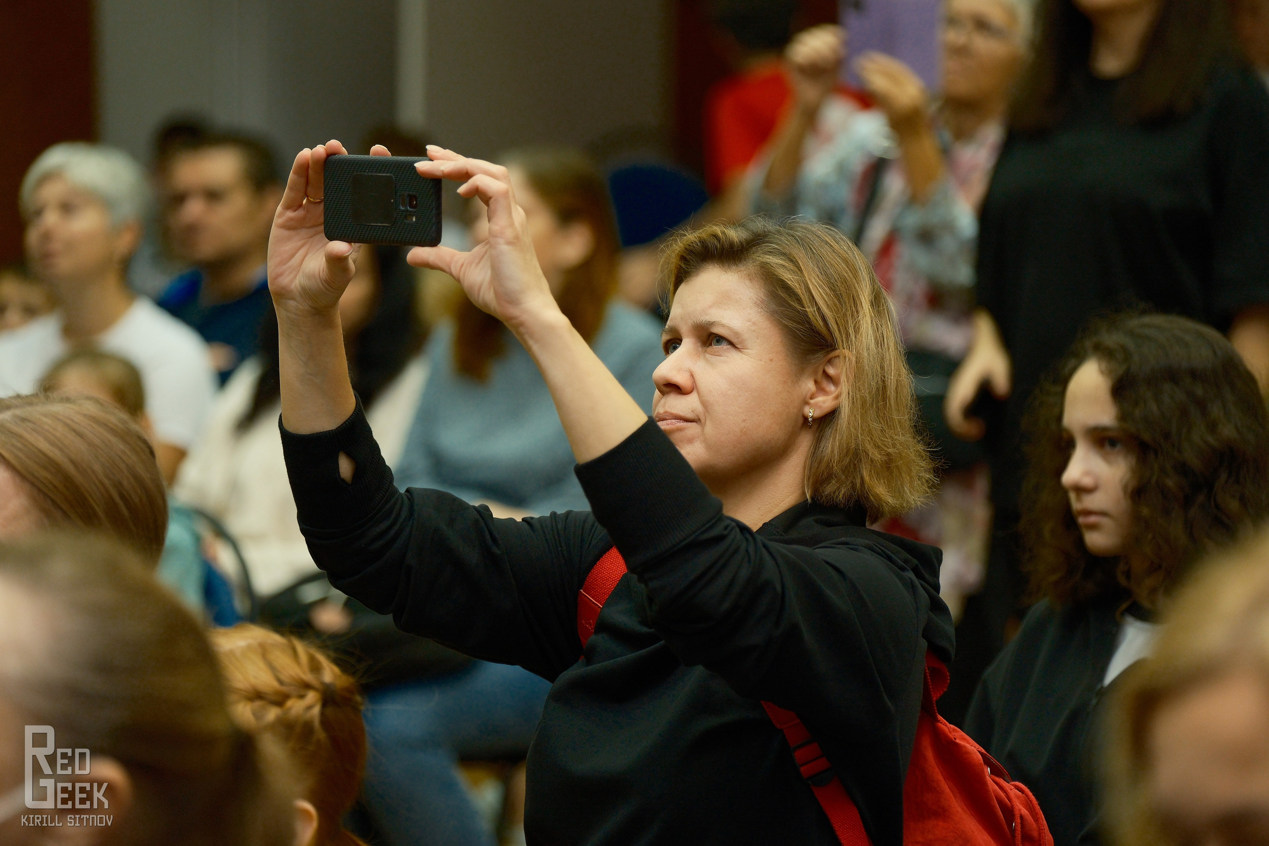 Девушка зрителем снимает на телефон выступление школьников на спортивном фестивале.