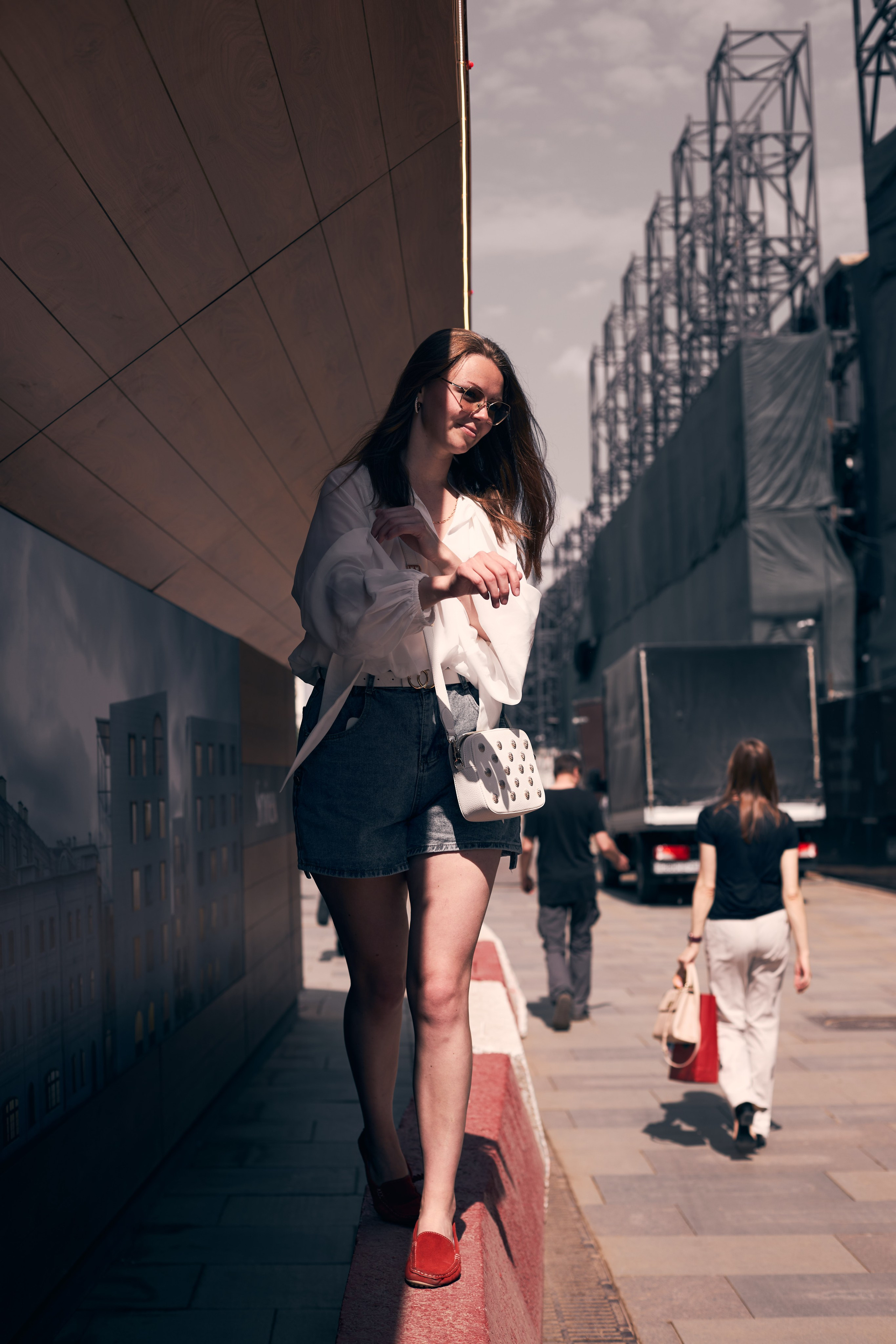 Красивая девушка с длинными волосами идёт по строительному бордюру. На лицо падает луч света