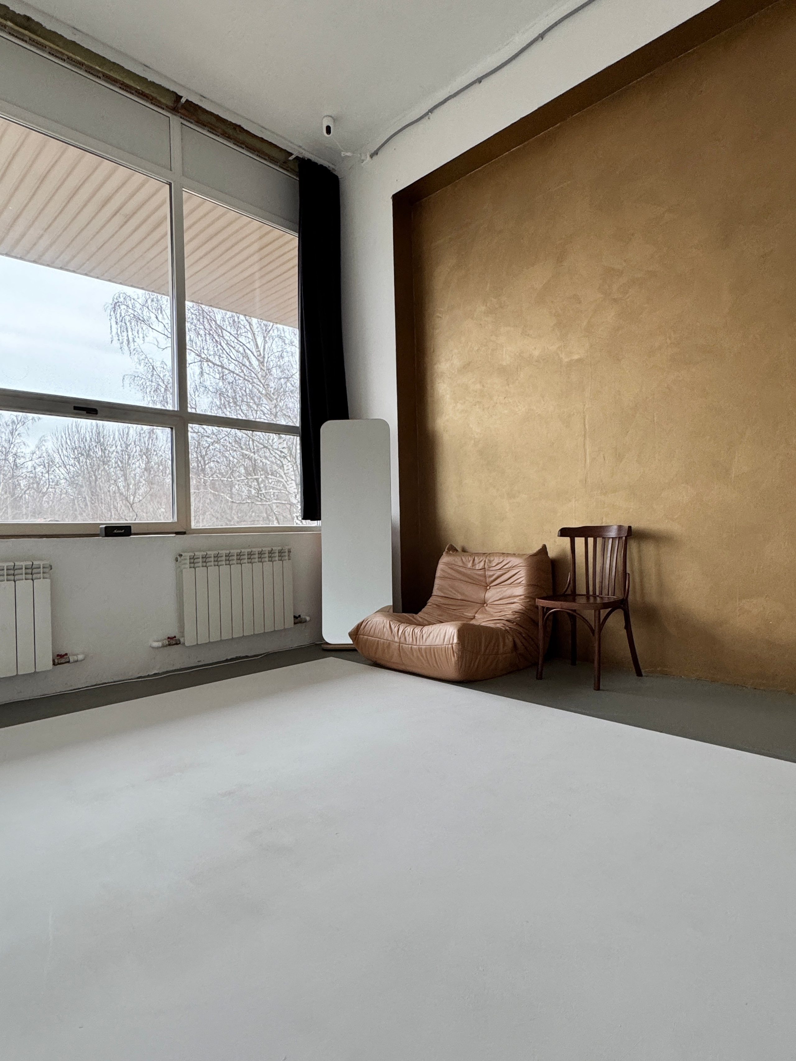 Большое окно, много света, декоративная стена золотого цвета, мягкое кресло, напольное зеркало, венский стул