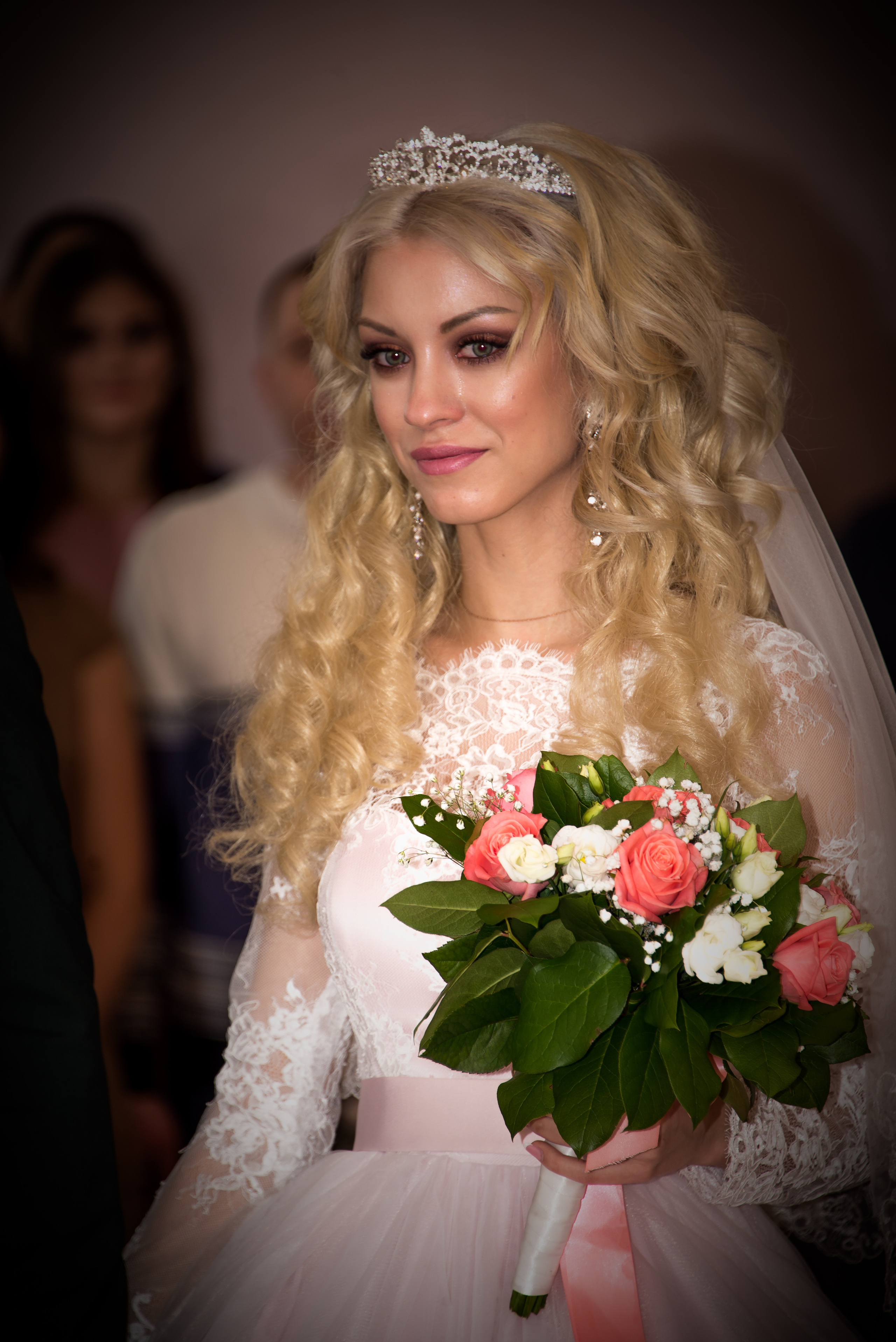 Счастливая невеста в свадебном платье держит букет цветов, вокруг нее друзья улыбаются на свадьбе