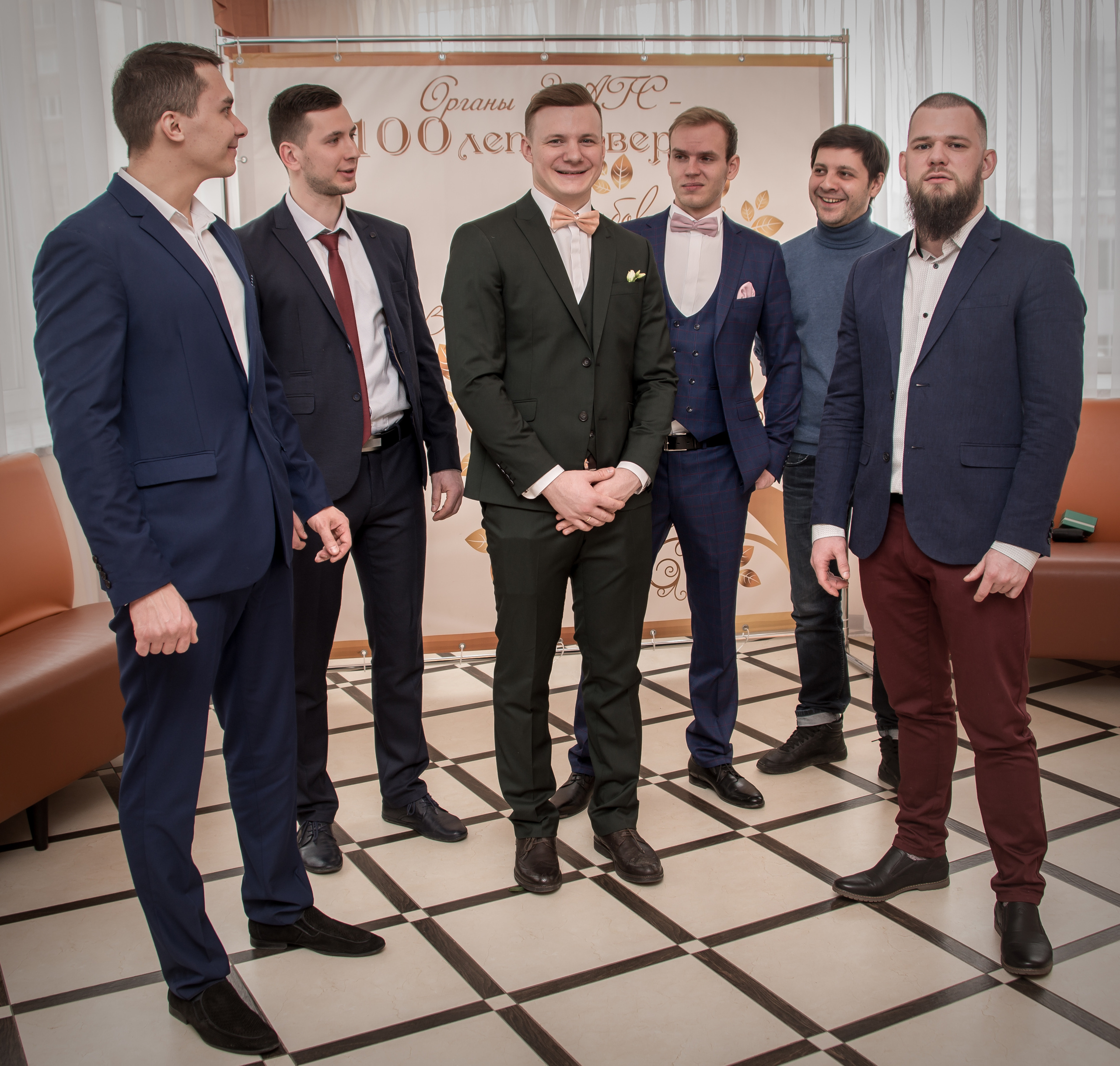 Лучшие друзья жениха и невесты в смокингах, улыбающиеся на фоне свадебного торжества