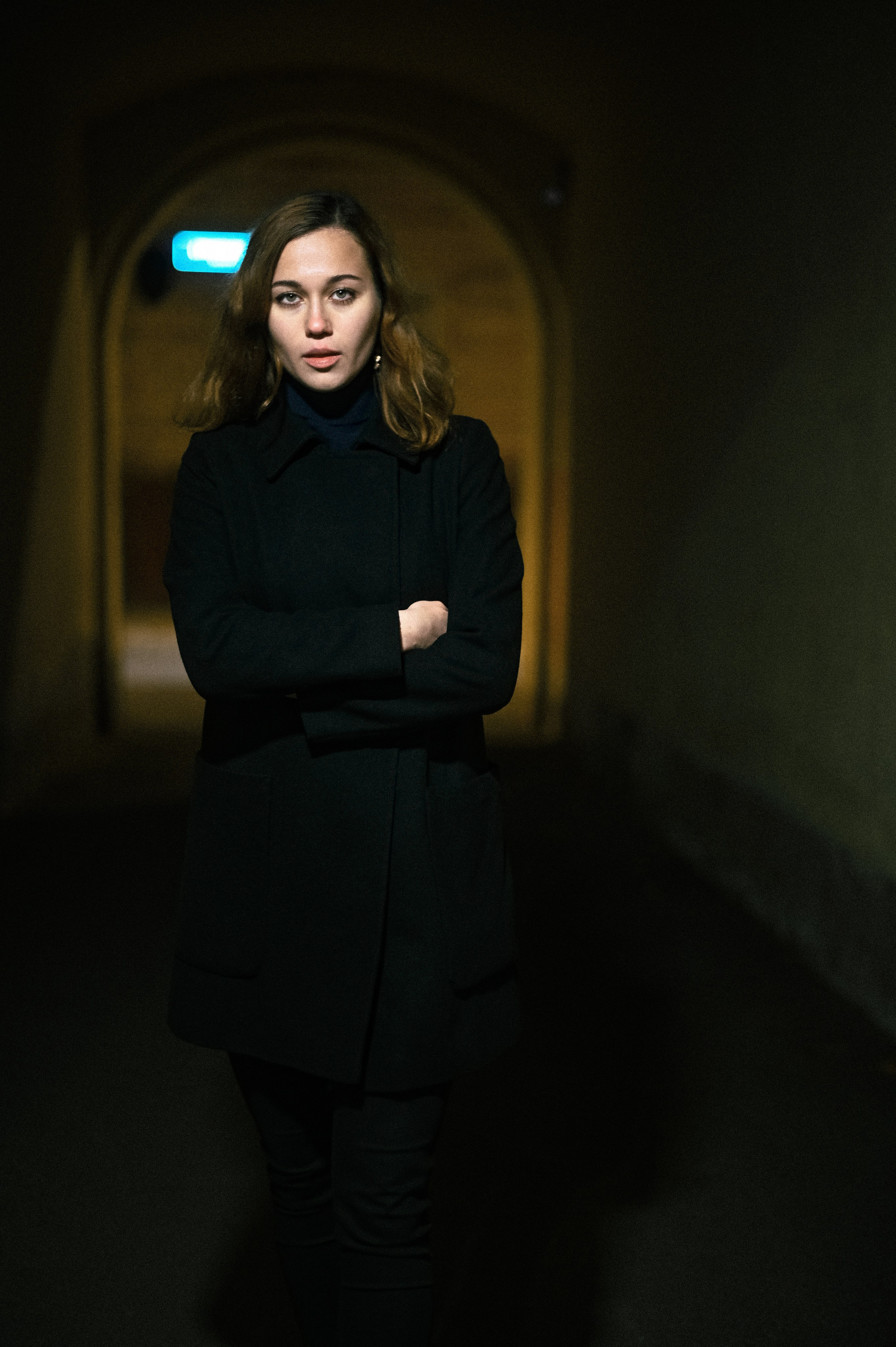 Портрет девушки с волнистыми волосами, одетой в чёрное пальто, снятый в ночном проходе в Москве.