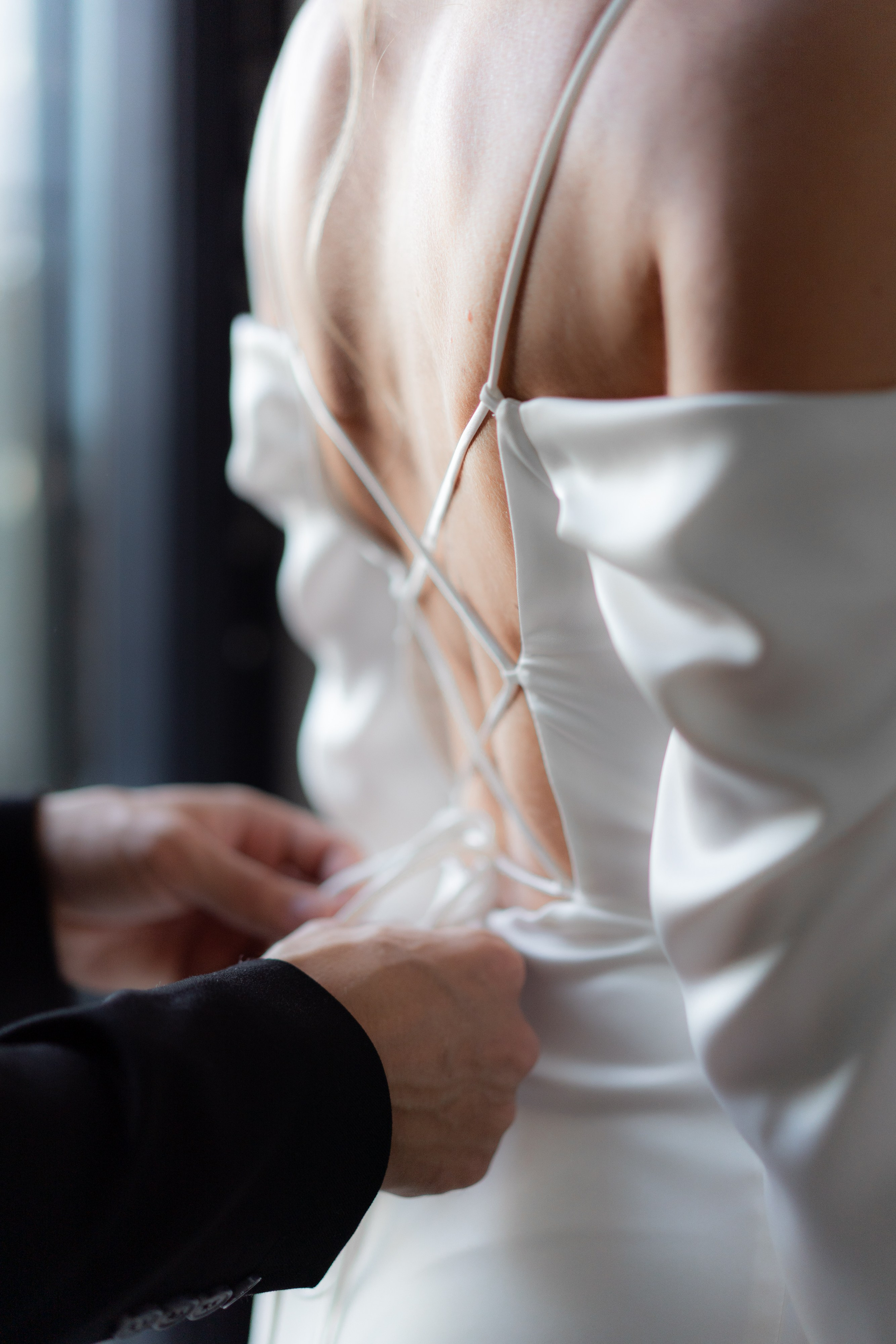 Спина невесты и руки жениха, которые завязывают корсет