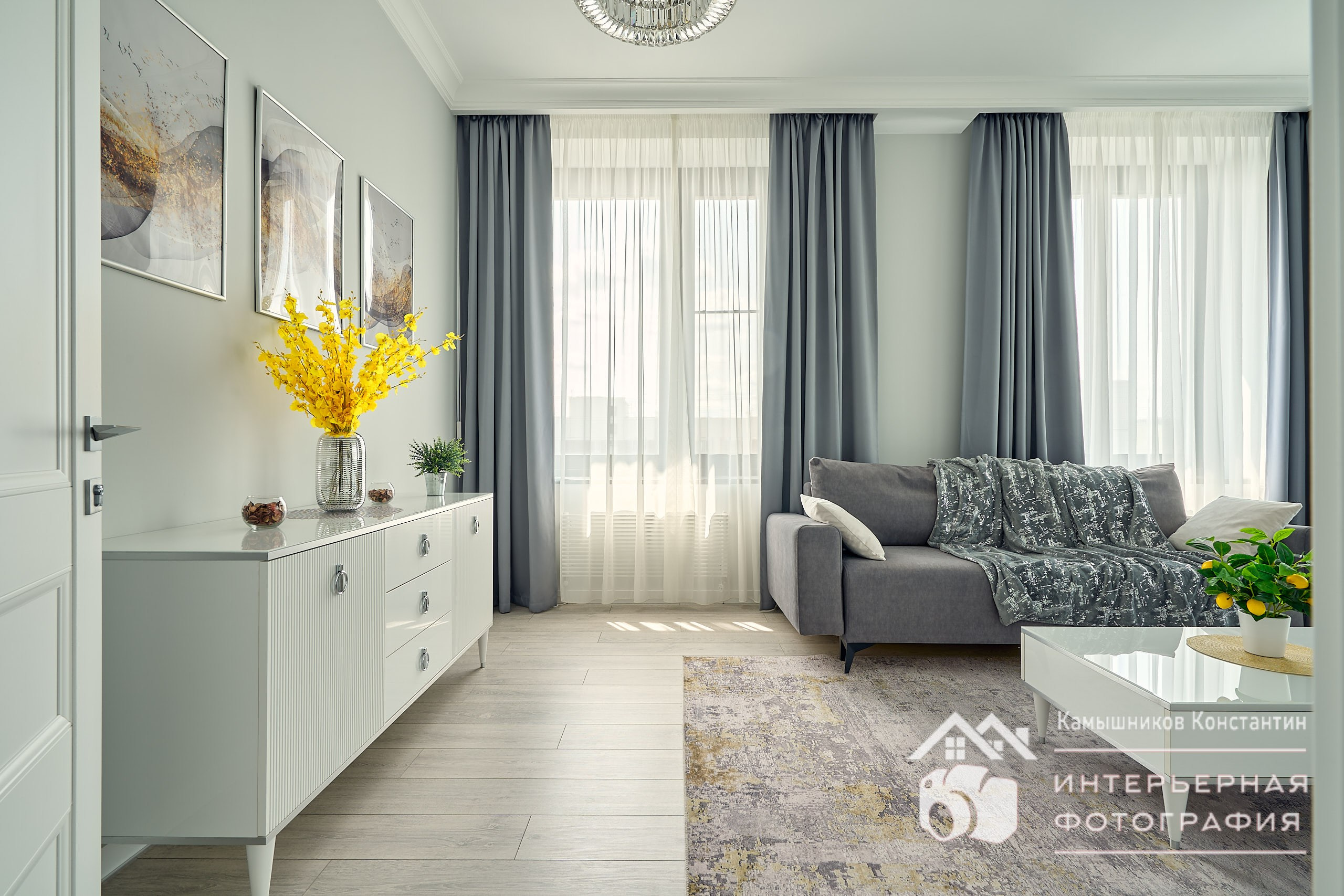 Часть интерьерной съемки квартиры бизнес-класса в Москве с комодом, декором, диваном и столиков в светлой гостиной, фронтальный план от входной двери