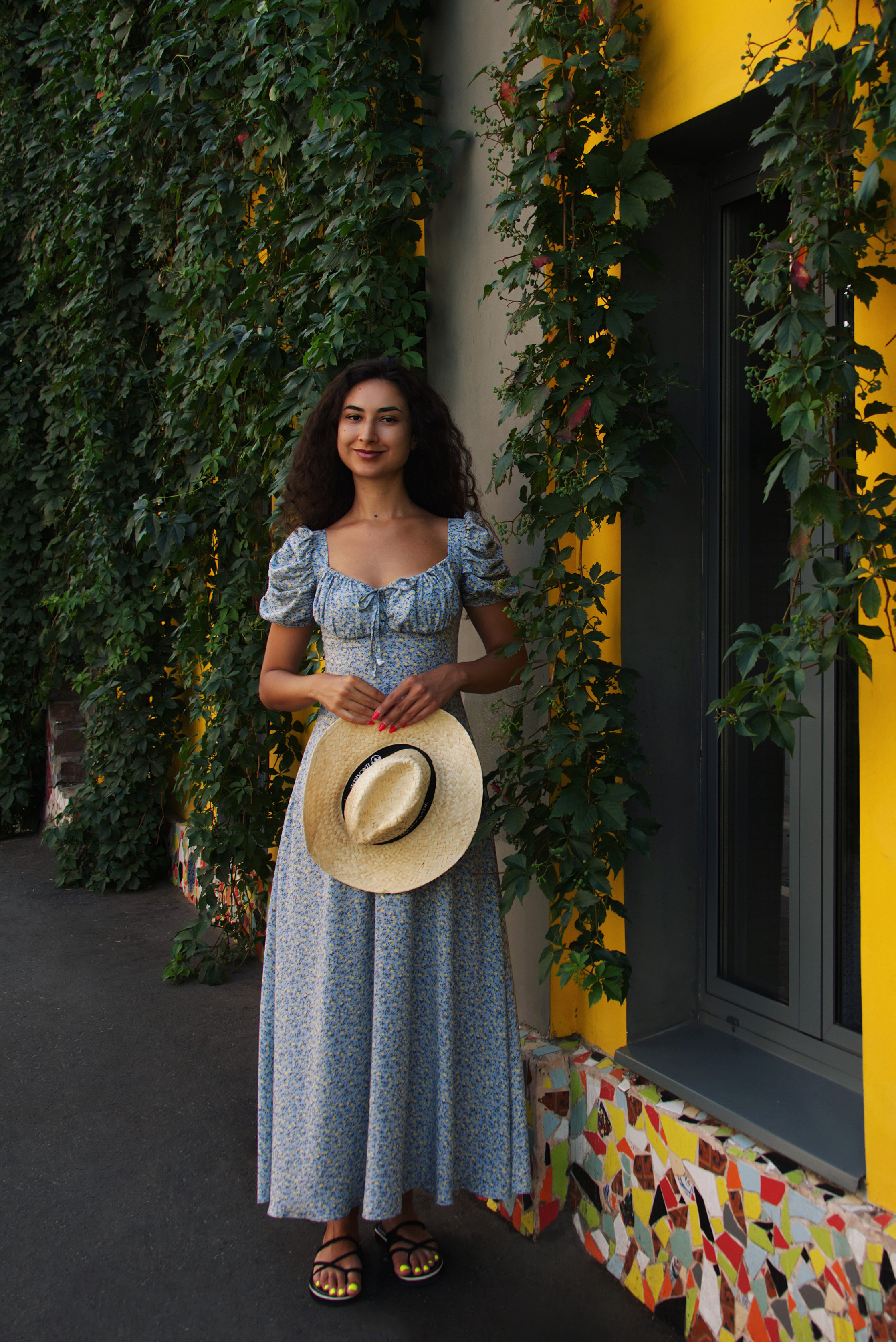 Летний портрет девушки в платье и со шляпой в руках на фоне улицы в центре Москвы.