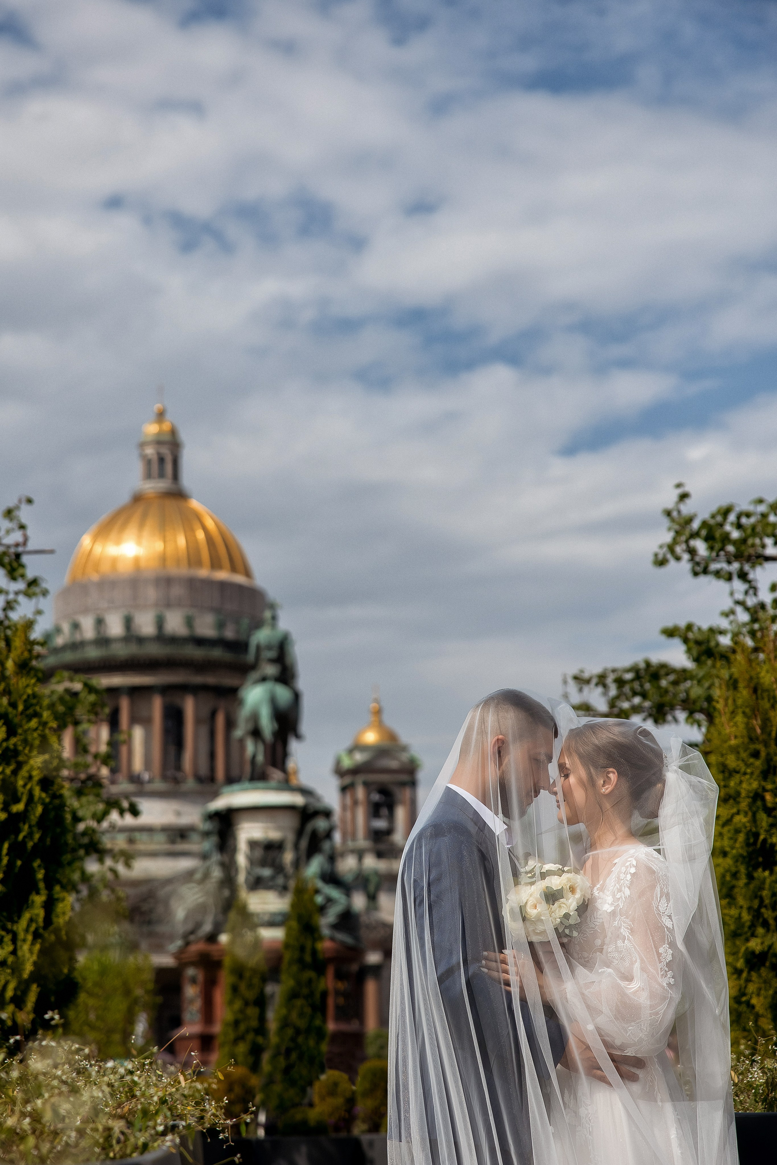 Портрет жениха и невесты, накрытых фатой на фоне купола Исаакиевского собора