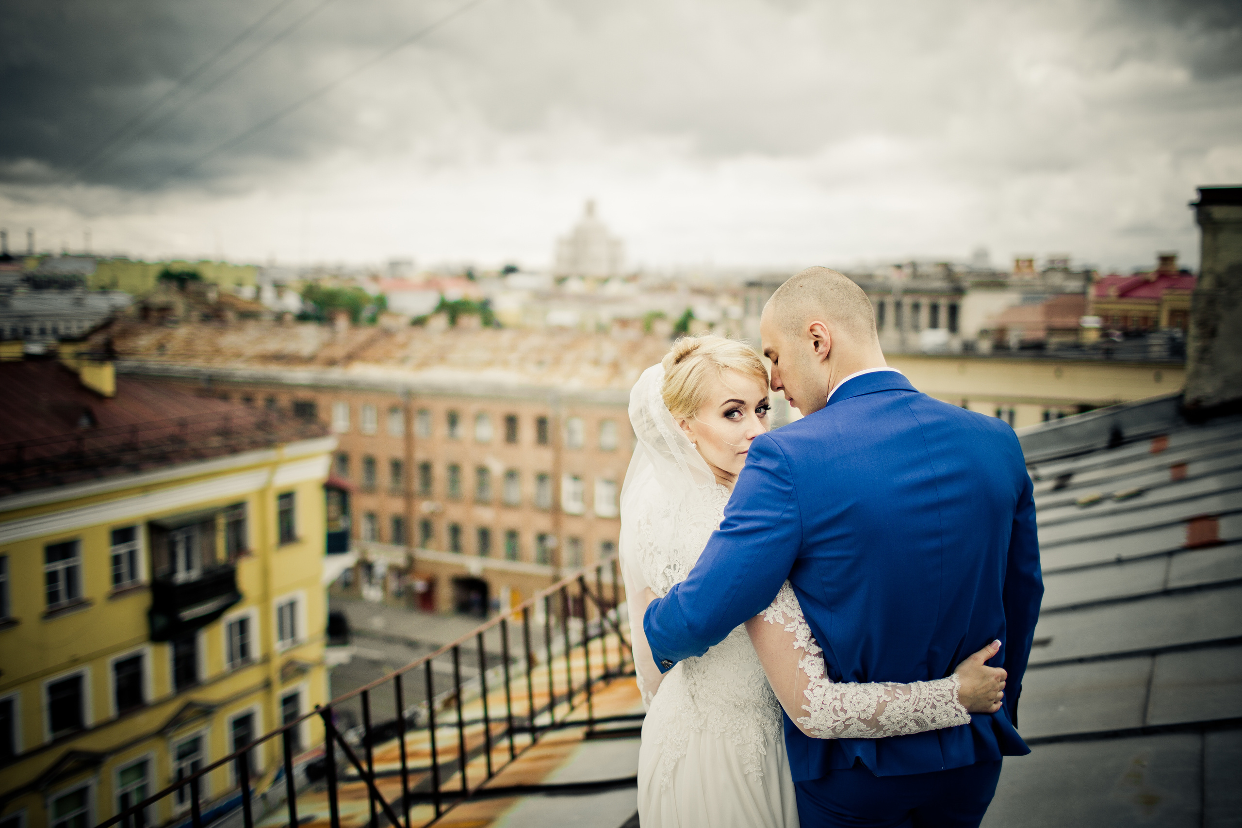 невеста выглядывает из-за плеча жениха на крыше с видом на город