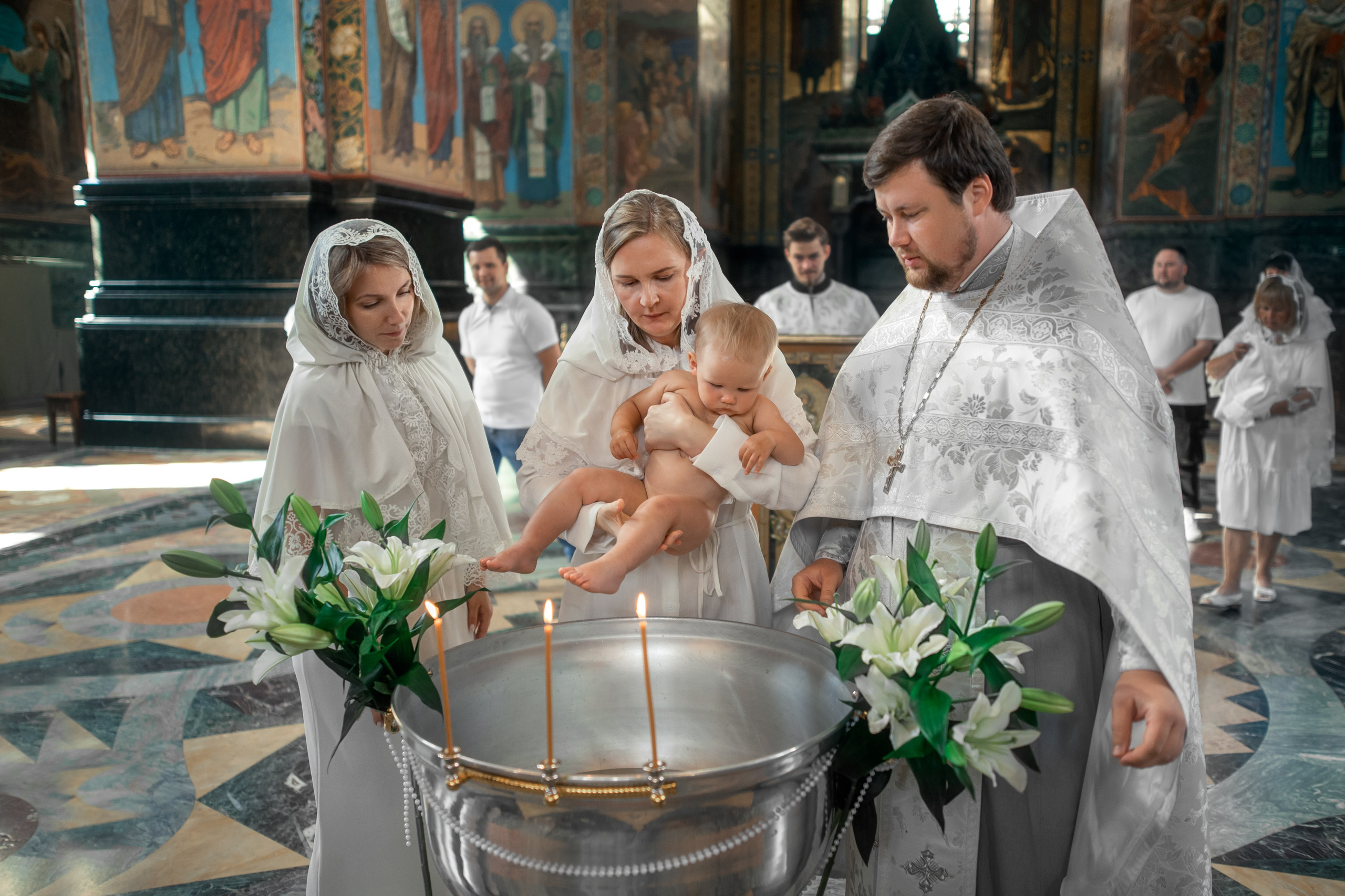 священник и крестная окунают девочку в купель