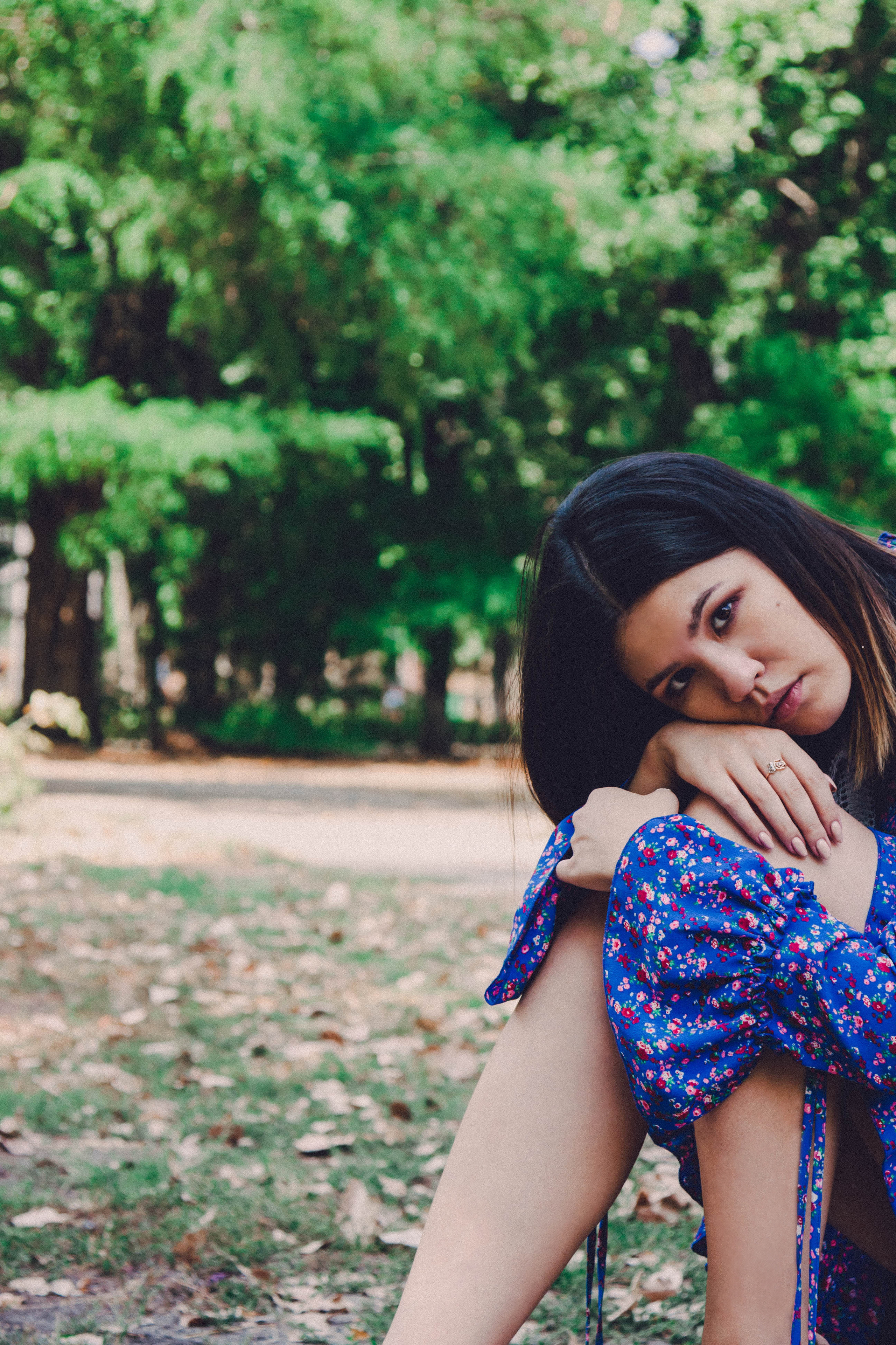 Девушка склонилась к колену. Грустная девушка в синей одежде на фоне зеленого леса или парка.