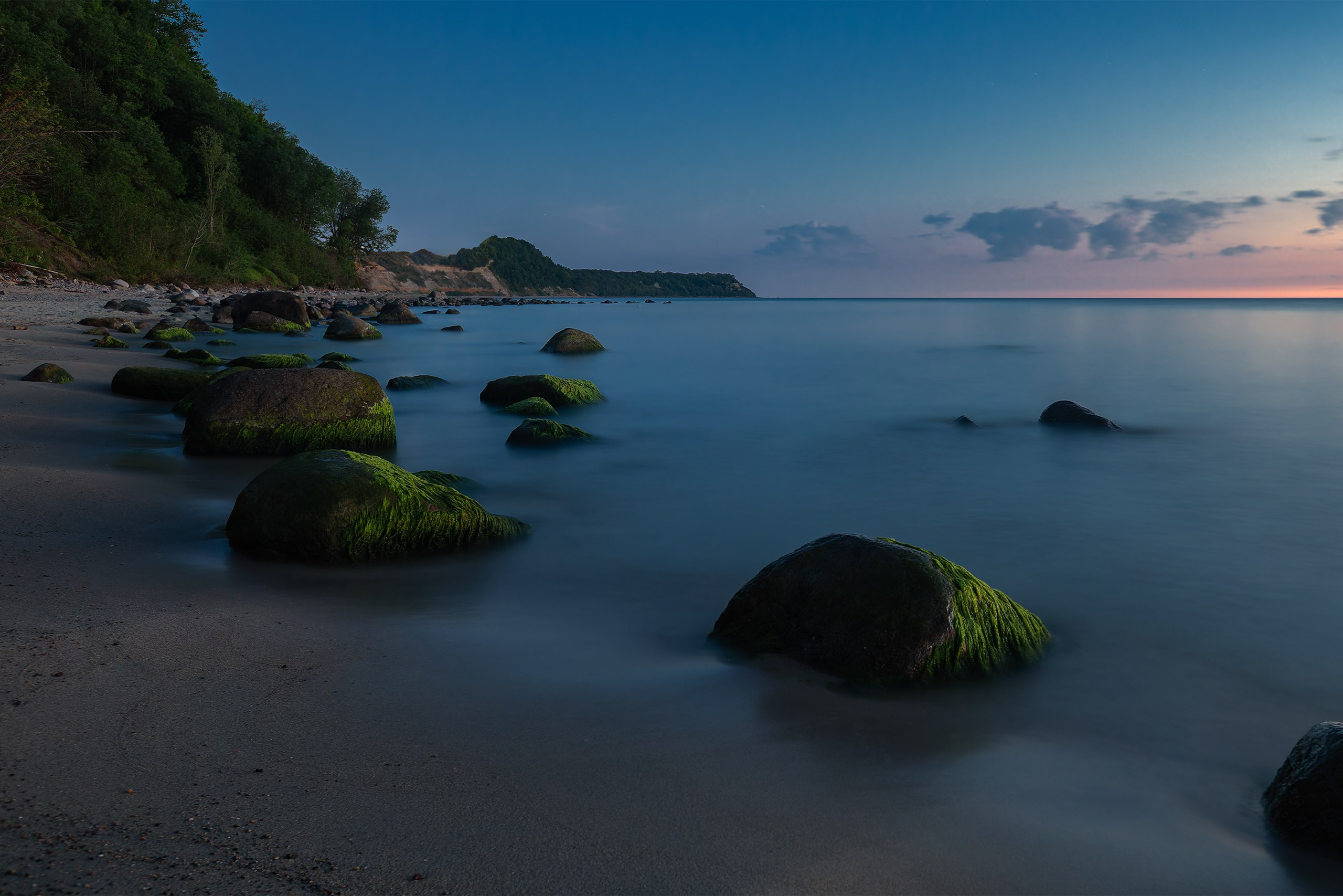 Scenic nightscape at Gross Kuhren showcasing large wet rocks and green seaweed on the coastline under a twilight sky.
